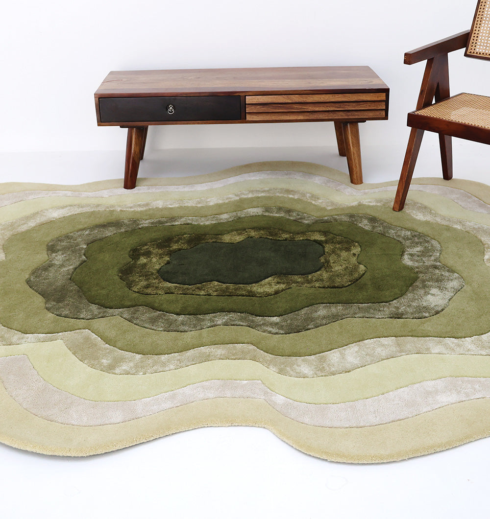 A modern living room with a wavy, green and beige layered area rug, a wooden coffee table with a drawer, and a wooden chair with a woven cane seat and backrest.