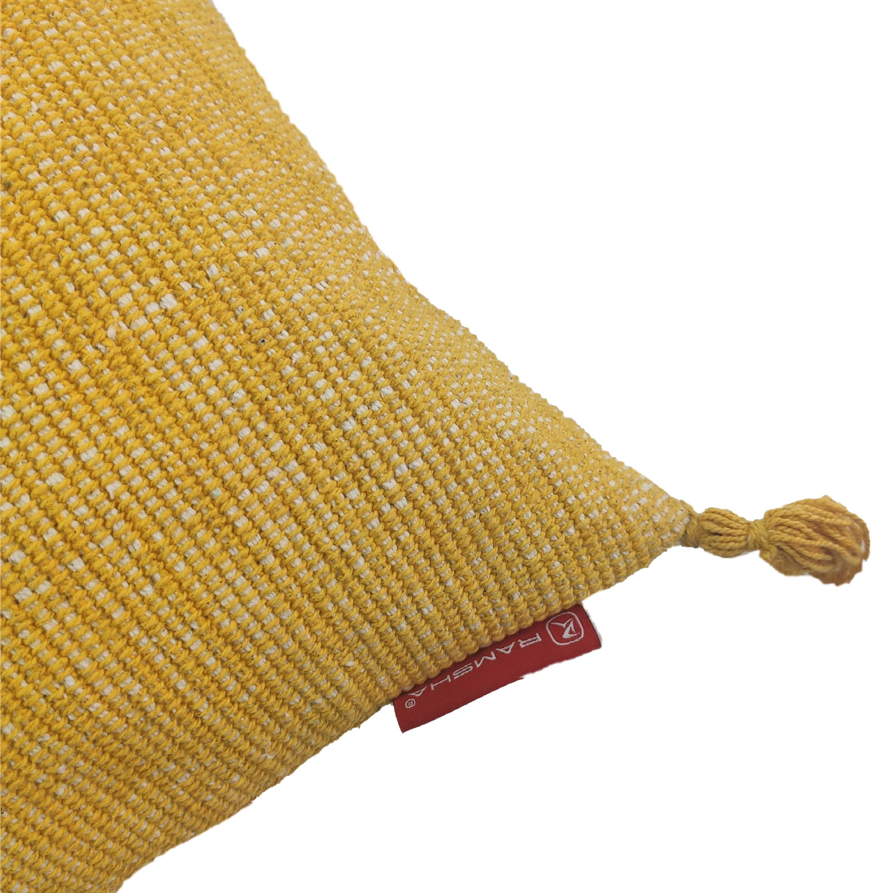 A close-up of the RAMSHA HOME Cotton Cushion With Fringes CS-133 in yellow cotton, featuring a braided tassel at the corner and a small red label. Set against a white background, this cozy cushion adds comfort and style to any space.
