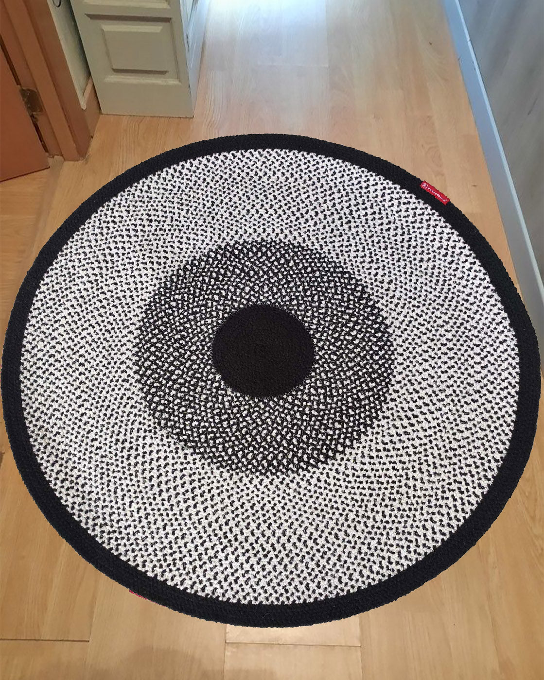 The RAMSHA HOME Black & White Color Round Braided Rug - BR 010 features concentric circles, adding a stylish accent to the light wooden floor near the hallway and cabinets.