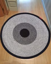 The RAMSHA HOME Black & White Color Round Braided Rug - BR 010 features concentric circles, adding a stylish accent to the light wooden floor near the hallway and cabinets.