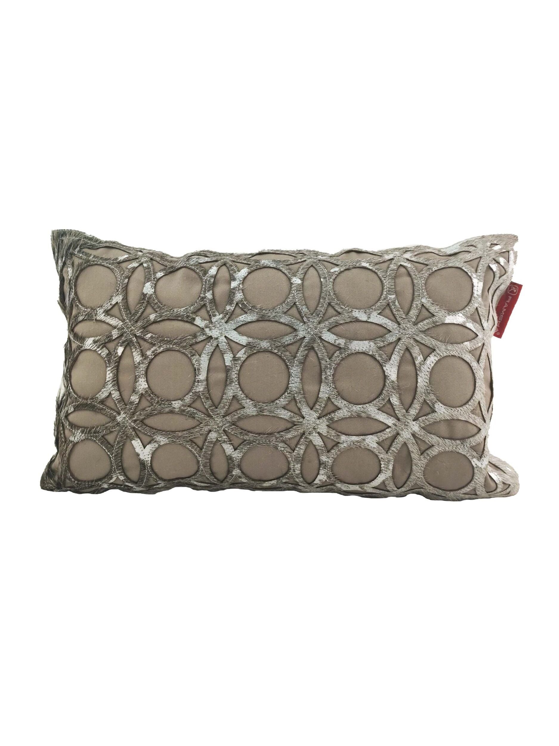 The RAMSHA HOME Leather Cushion CS-100 is a rectangular beige pillow with a textured pattern of interlocking circles and ovals, a slightly raised design, durable construction, and a small red tag on the right side.