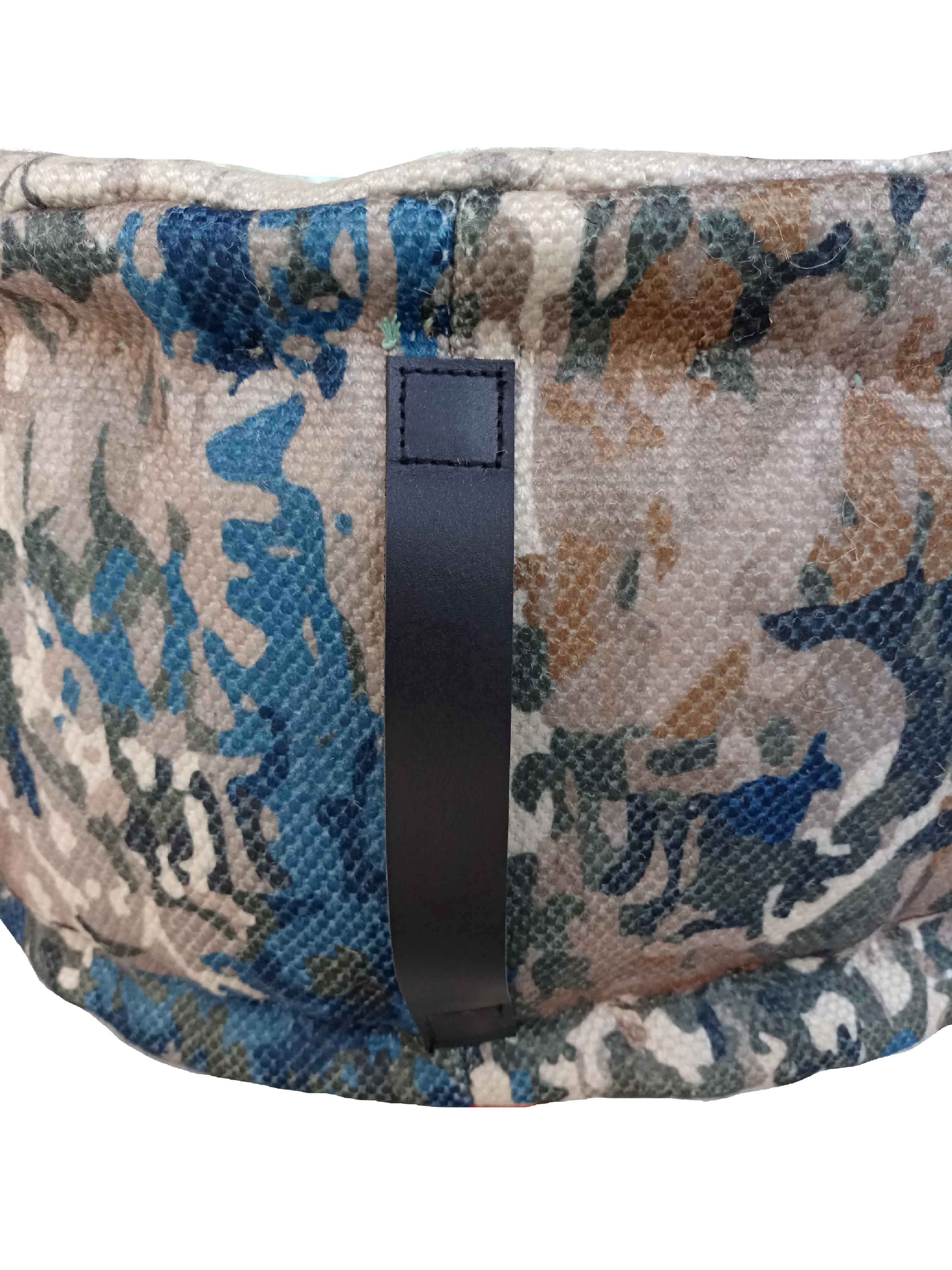 A close-up of the Printed Multi Color Pouf With Leather Handle PF-030, showing its blue, brown, and beige camouflage fabric with a stitched black leather handle. Ideal for home decor accents. The background is white.