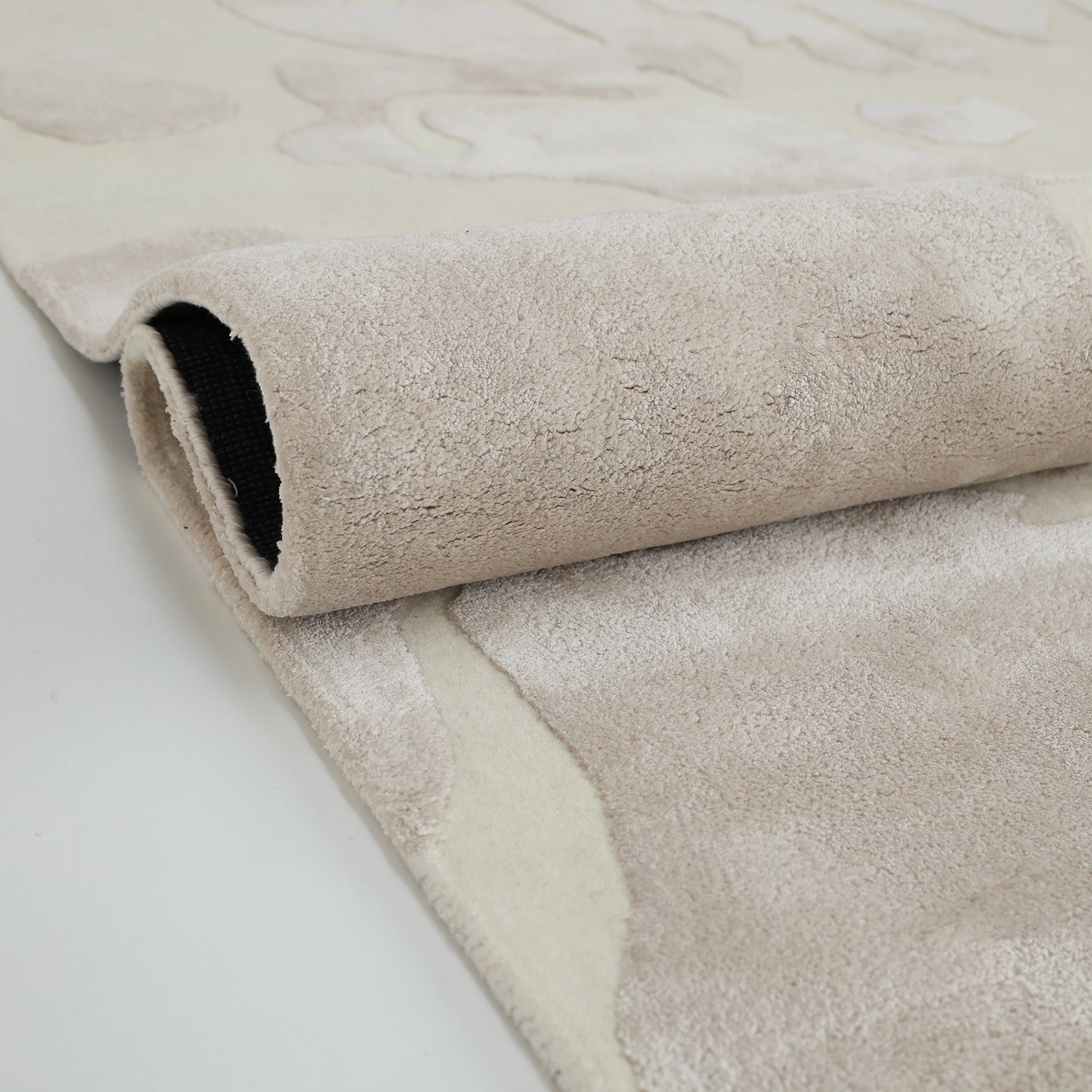 A close-up of the RAMSHA HOME Multi Color Handmade Area Rug - HTWV-132, partially rolled to reveal its soft textured surface and black backing, handtufted and displayed on a smooth, light-toned floor.