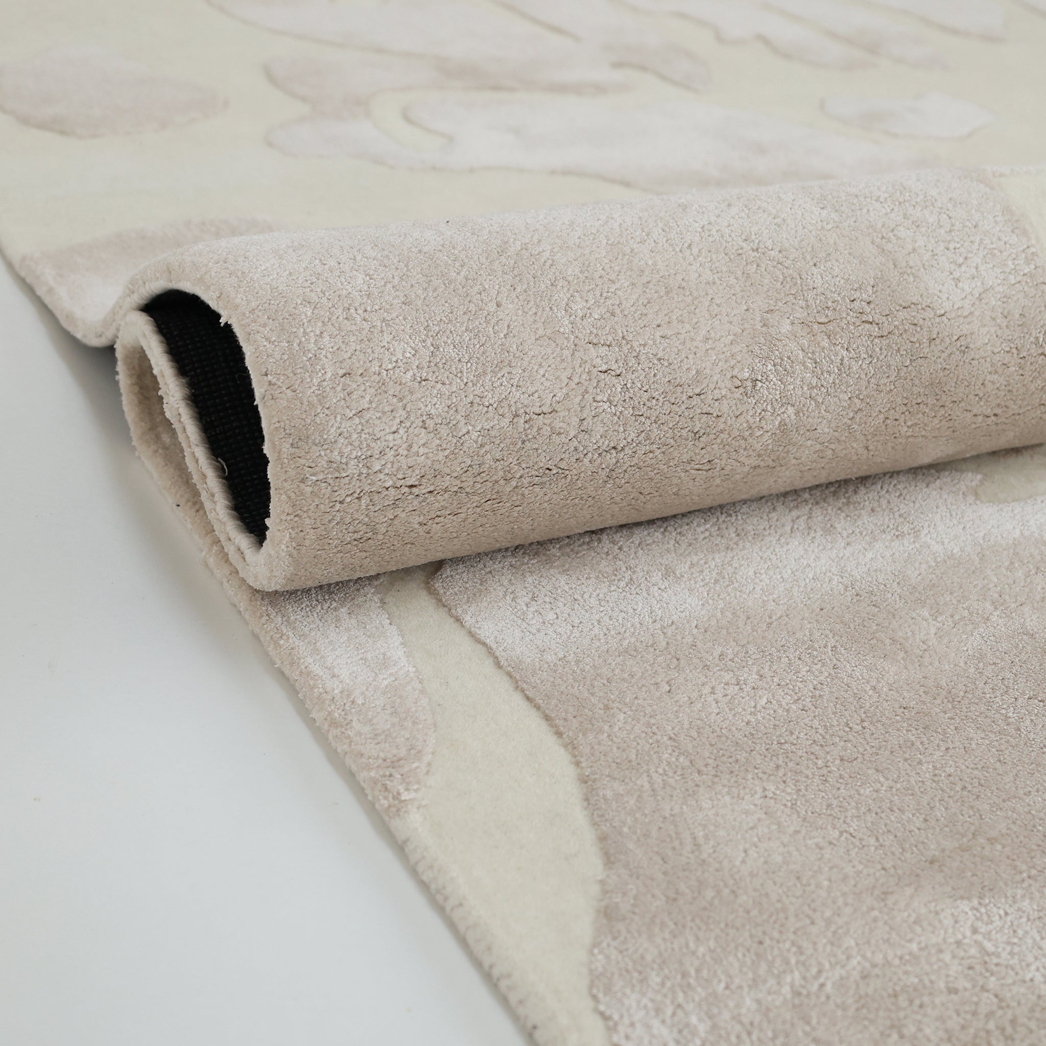 A close-up of the RAMSHA HOME Multi Color Handmade Area Rug - HTWV-132, partially rolled to reveal its soft textured surface and black backing, handtufted and displayed on a smooth, light-toned floor.