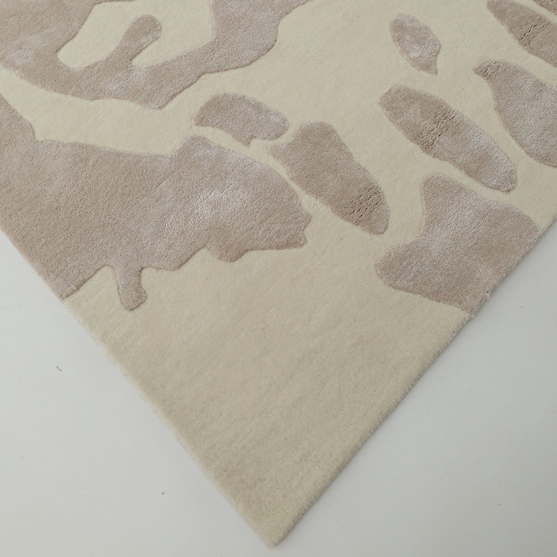 A close-up of the RAMSHA HOME Multi Color Handmade Area Rug - HTWV-132 displays its soft, textured beige surface with an intricate light brown pattern as its handtufted corner rests elegantly on a white floor.