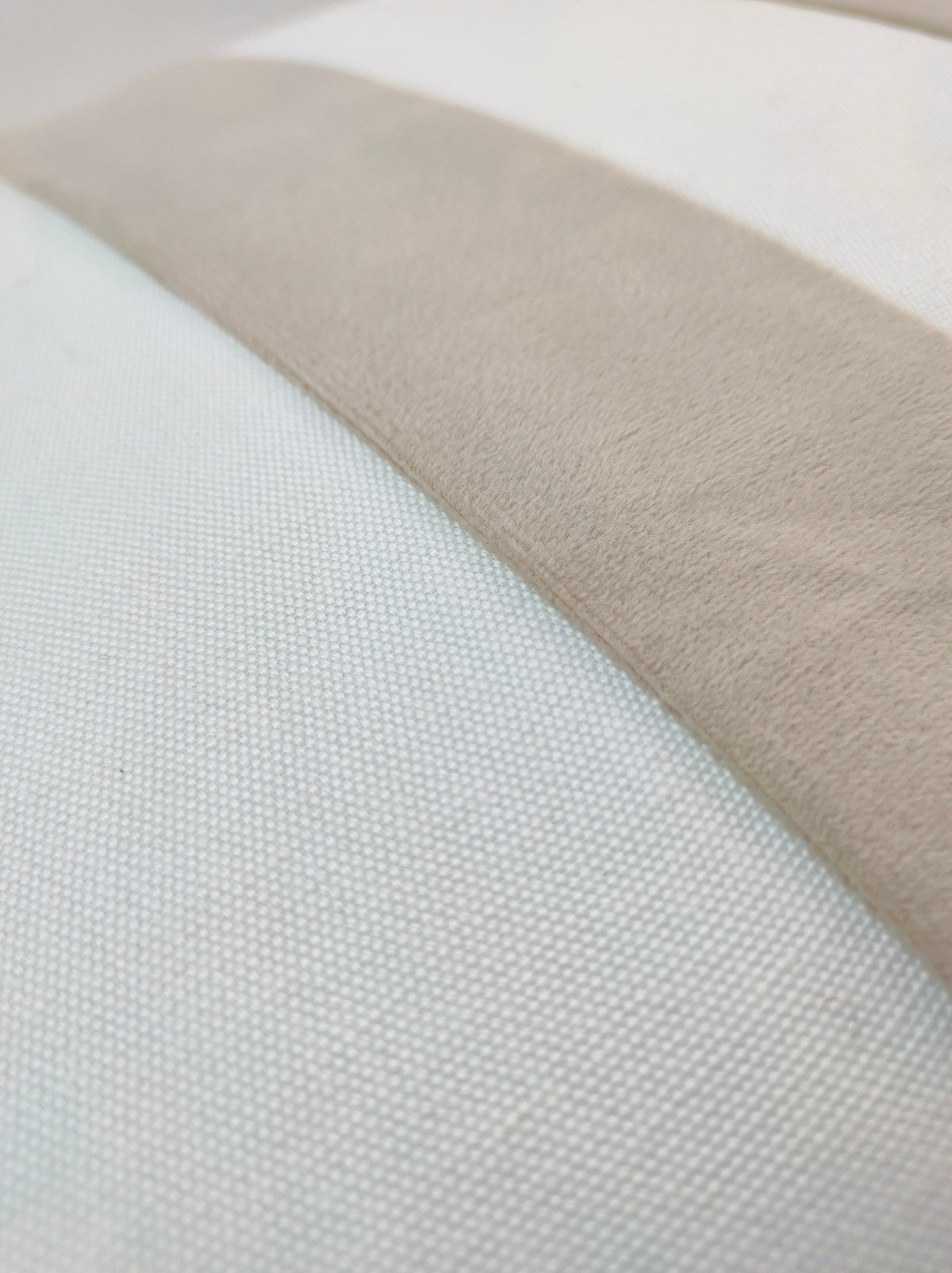 Close-up of the RAMSHA HOME White & Light Beige Color Cushion CS-136, featuring a soft beige suede strip set diagonally on a textured white background, highlighting its contrasting textures and subtle, inviting hues.