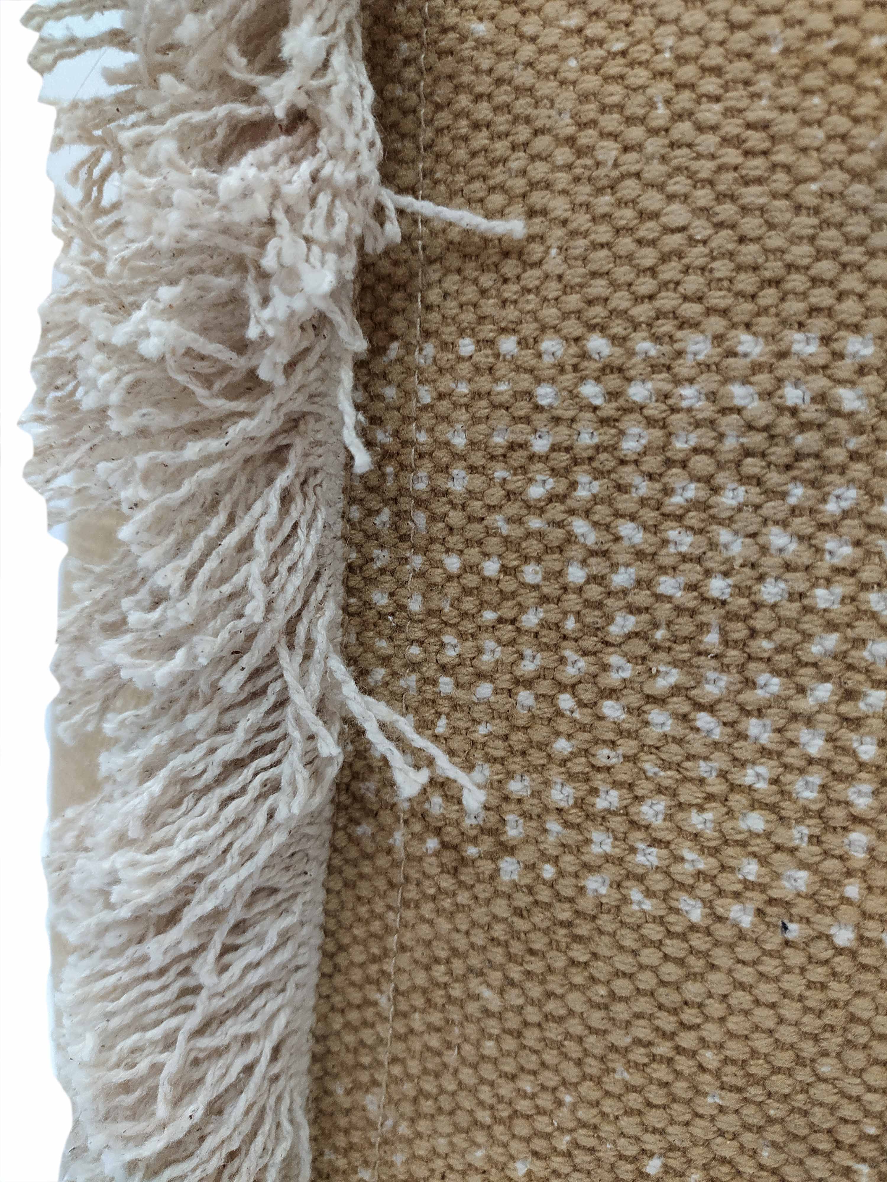 Close-up of a woven beige fabric with small white dots and a cream fringe, ideal as an accent on the RAMSHA HOME Pouf With Leather Handle PF-049 in black cotton.