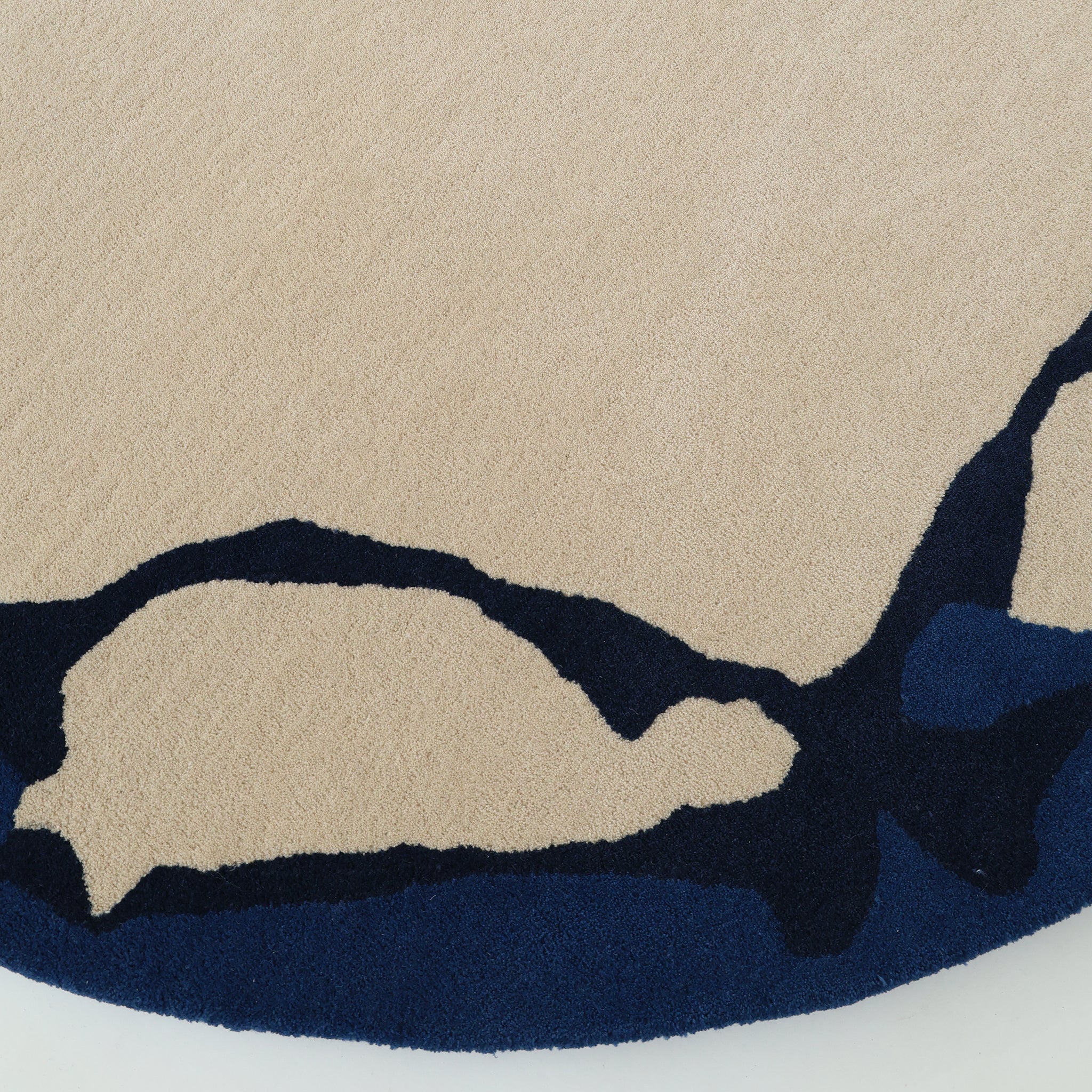 A close-up of the RAMSHA HOME Round Handmade Hand Tufted Carpet HTW-64, featuring irregular dark blue abstract patterns along the edge—an eye-catching modern wool rug perfect for contemporary spaces.