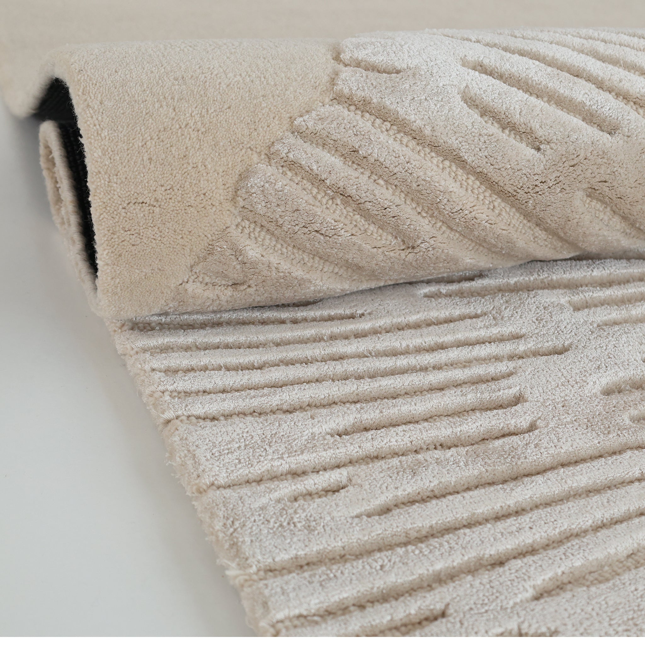 A close-up of the RAMSHA HOME Hand-Tufted Carpet For Home Decor HTWV-76 in beige, featuring a raised linear pattern and a folded corner highlighting the plush surface and thickness of this contemporary wool rug.