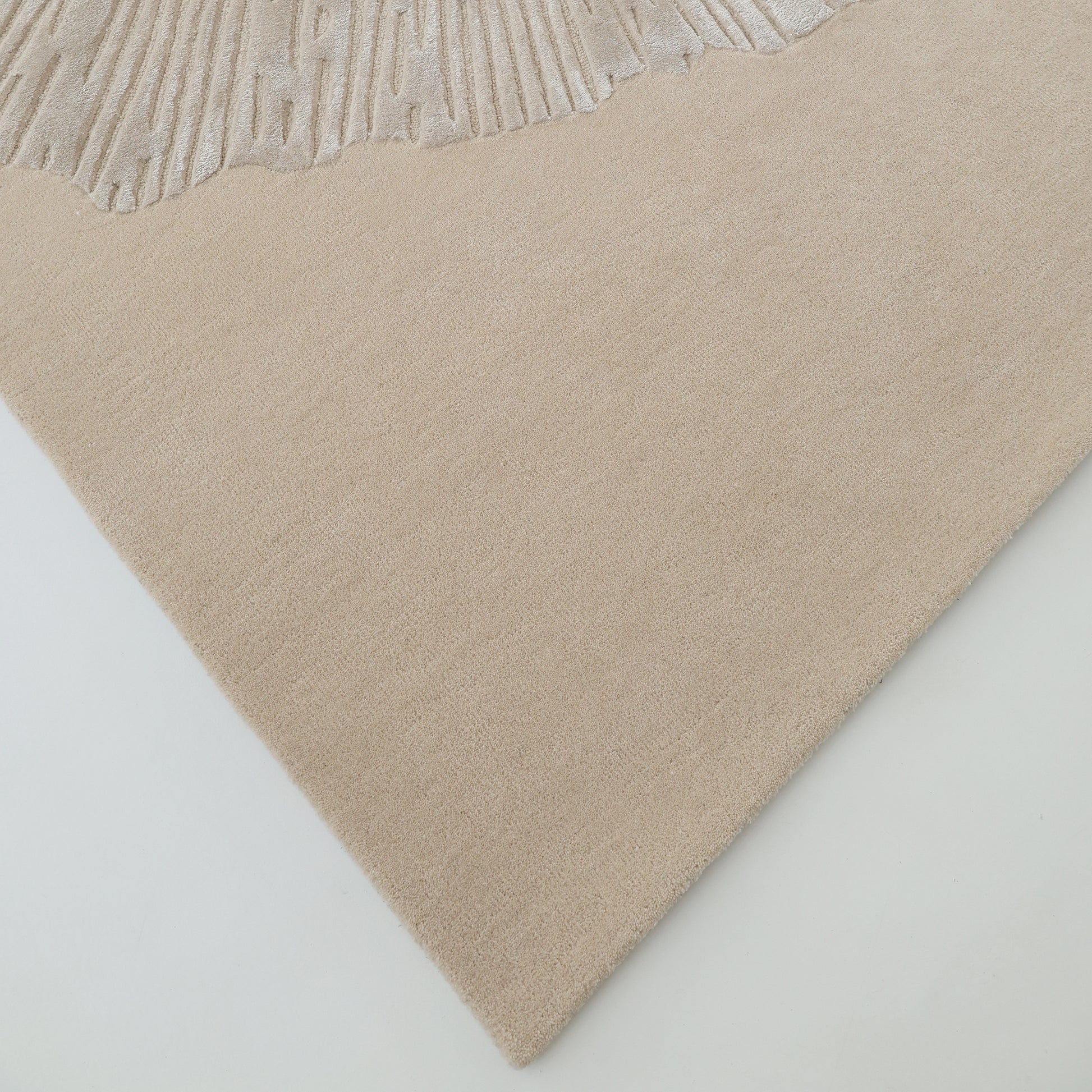 A close-up of the RAMSHA HOME Hand-Tufted Carpet For Home Decor HTWV-76 in beige, showcasing its textured wavy edge pattern, displayed on a light floor.