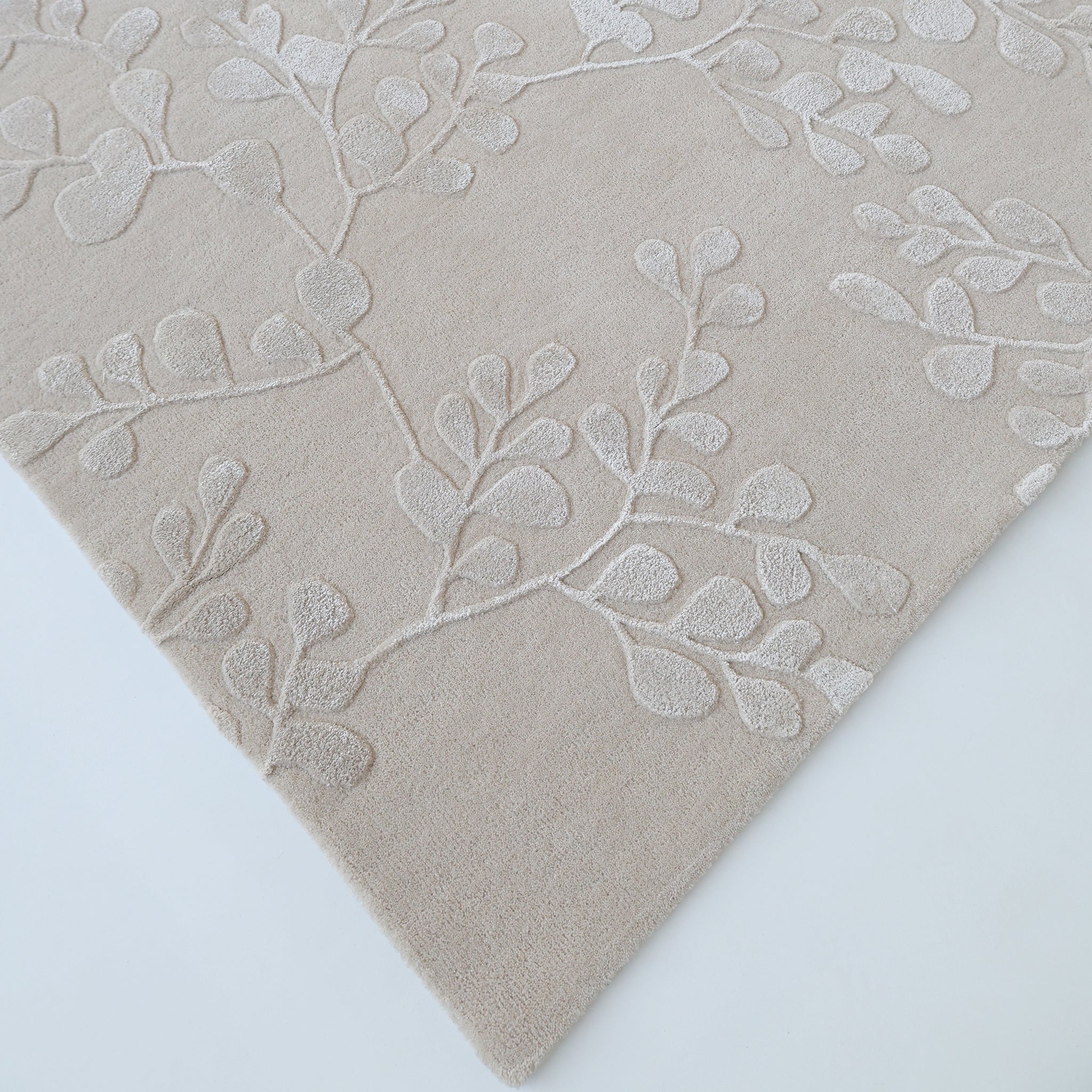 The RAMSHA HOME Artisan Handmade Decorative Area Rug – HTWV-116 features a beige botanical design with a raised, textured leafy branch pattern in a lighter shade, displayed at an angle on a white background.
