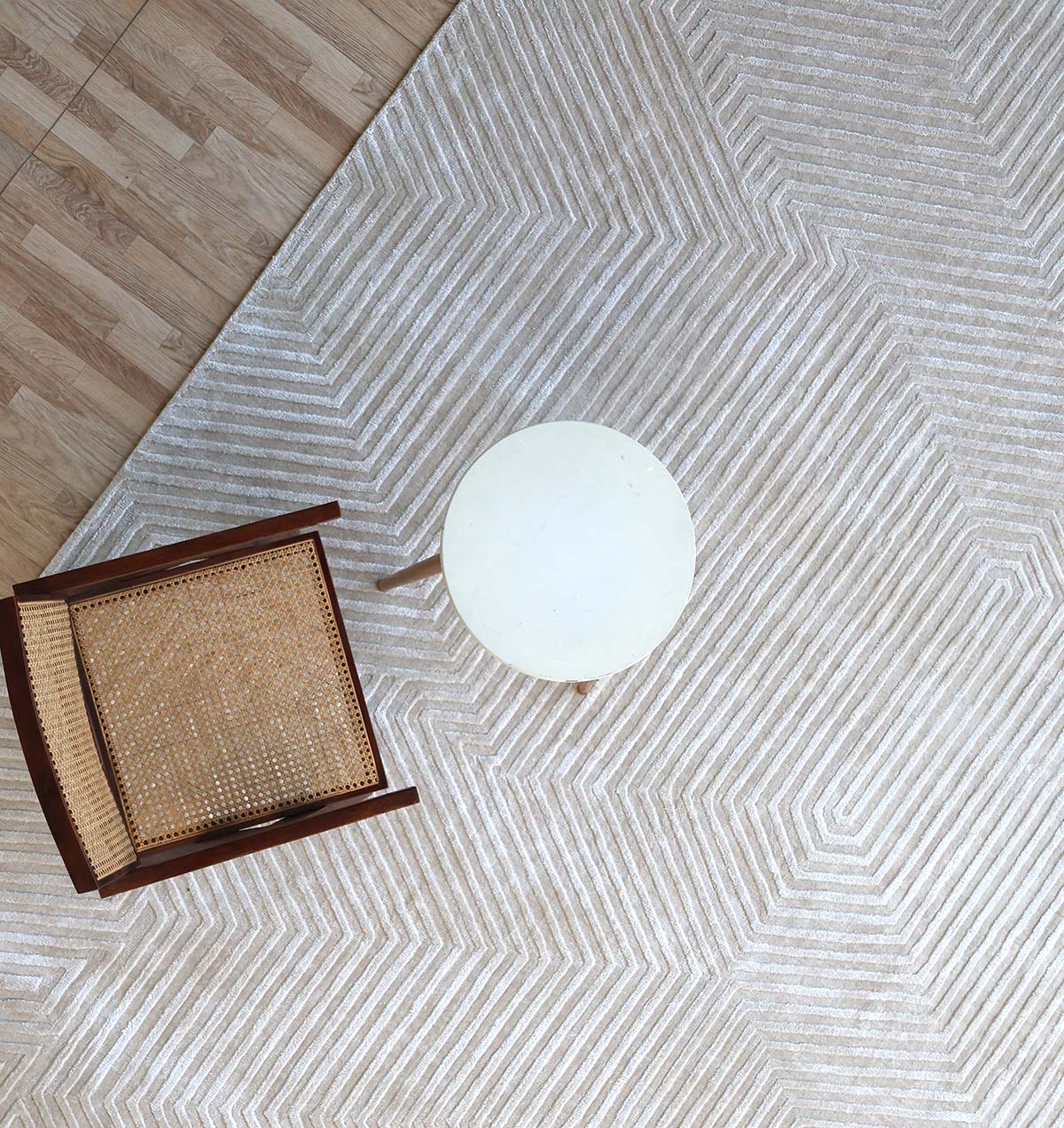 Overhead view of a wooden chair with a woven seat beside a small round white table, both set on the Geometric Hex Line Patterned Handmade Area Rug - LKH-08 atop a wooden floor.