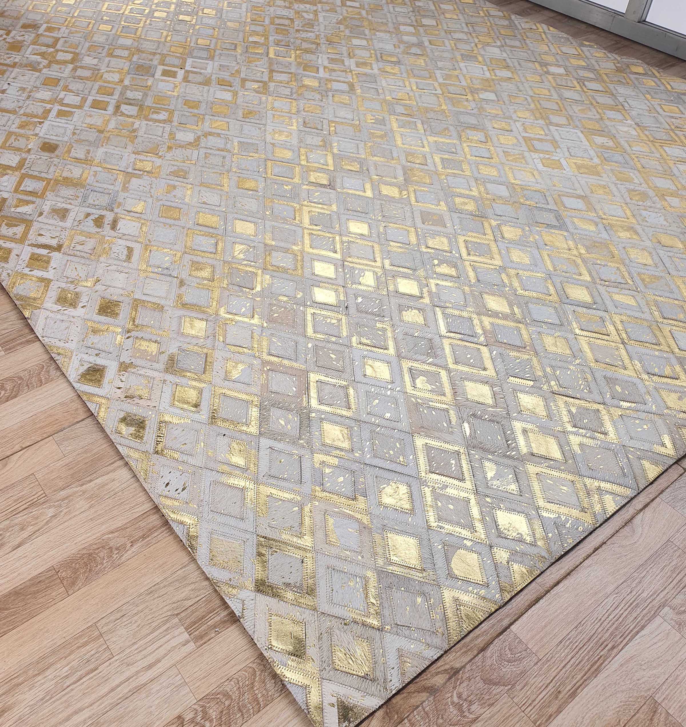 A close-up of the RAMSHA HOME Handmade Diamond Patterned Leather Rug LR-010, featuring a gold and beige geometric diamond pattern, is shown on a light wood floor near the corner of a room with a white wall and cabinet.
