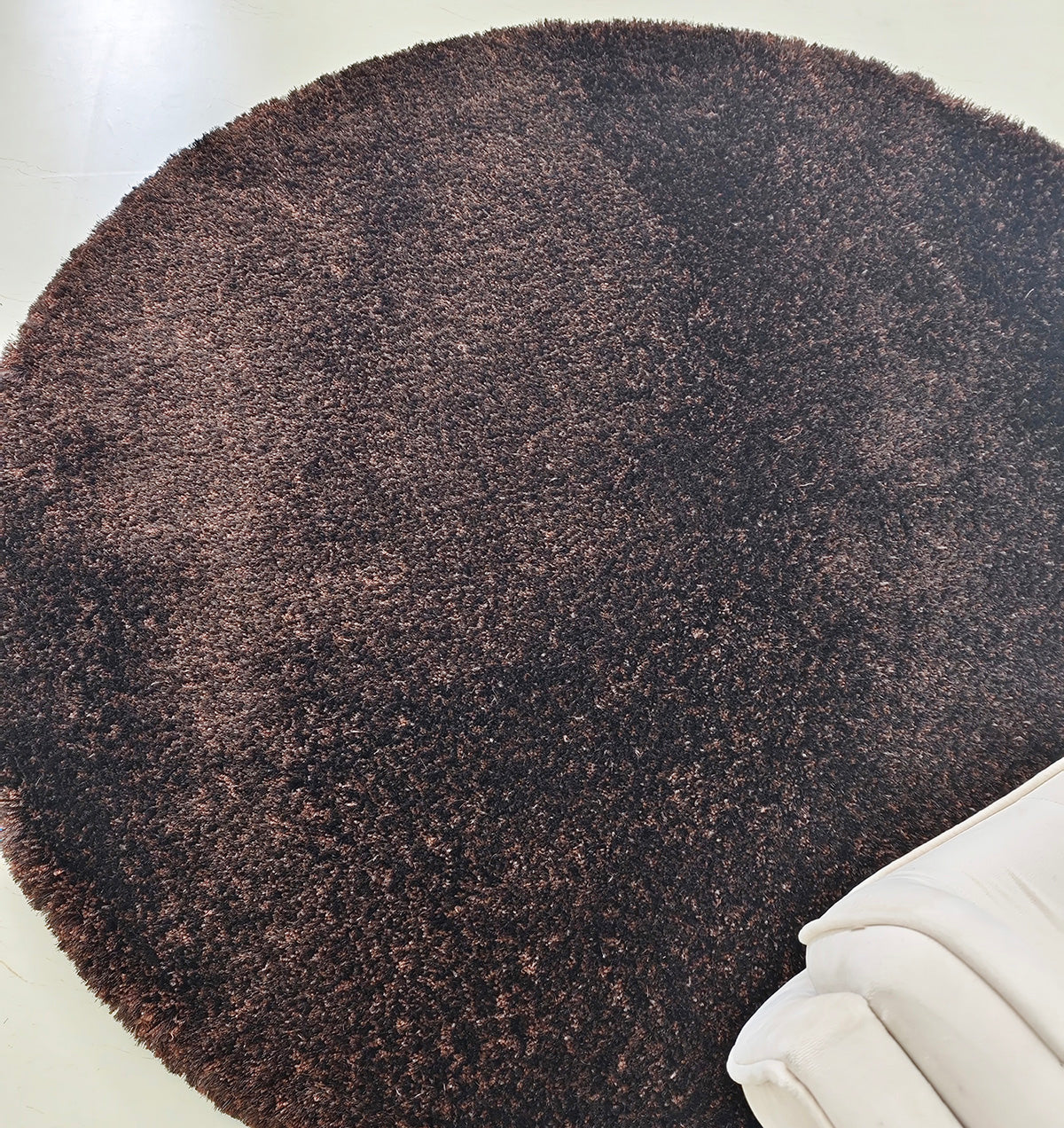 The RAMSHA HOME Fluffy Shaggy Round Shape Area Rug SG 04 in brown sits on a light floor, with the edge of a light beige sofa visible in the lower right corner.