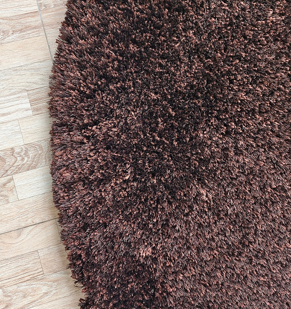 A close-up of the RAMSHA HOME Fluffy Shaggy Round Shape Area Rug SG 04 - Brown shows its plush, dense fibers creating a cozy contrast against the smooth, light wooden floor.