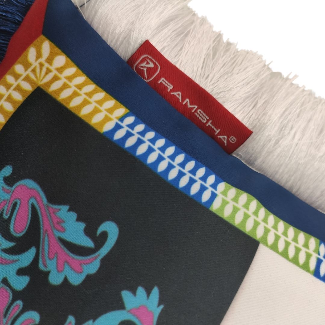 A close-up of a colorful Area Cushion With Filler Multi Color CS-064 by RAMSHA HOME features a decorative pattern, white fringe for added coziness, and a partially covered red RAMSHA HOME label.