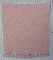 The Pink Color Cotton Throws for Sofa TAL 042 (125x150 cm) by Ramsha Home offer breathable comfort and a textured feel, with fringed tassels, elegantly displayed against a light gray wooden background.