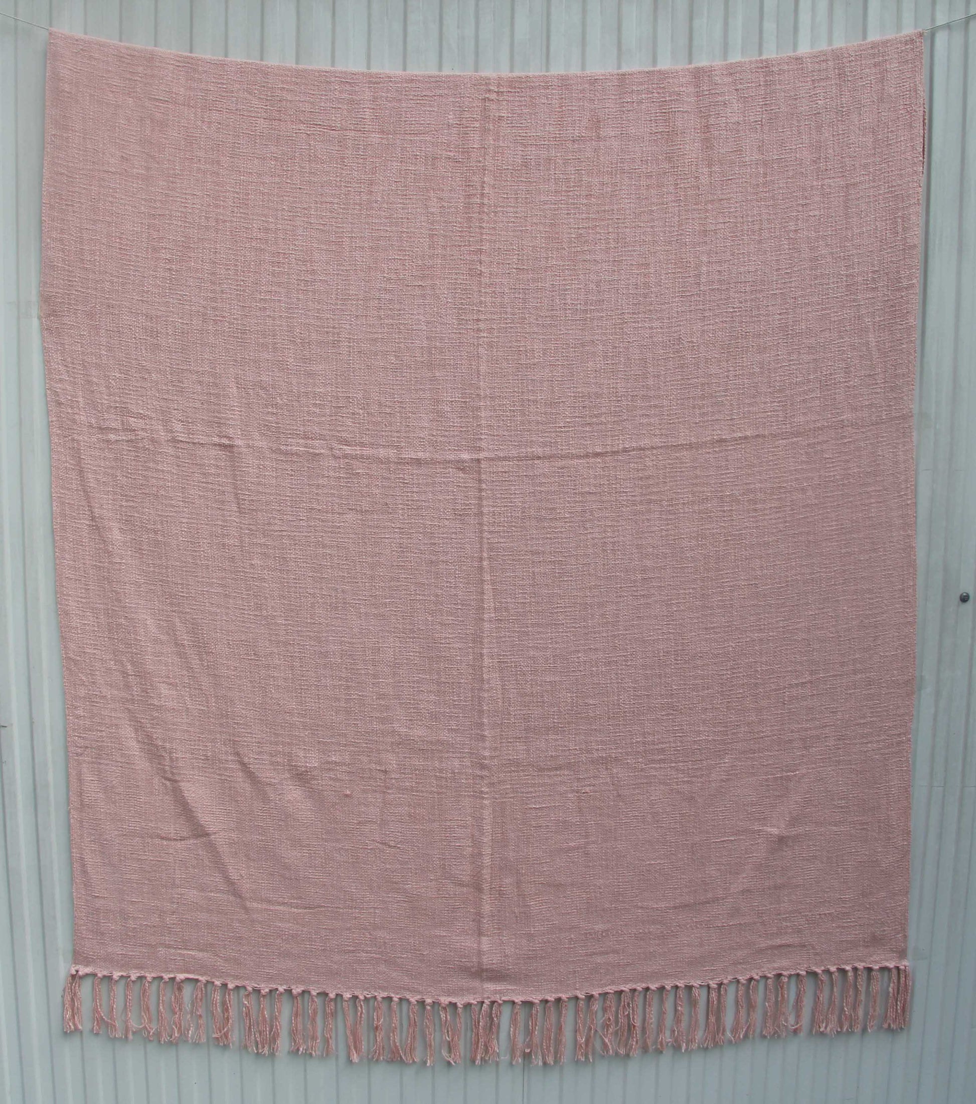 The Pink Color Cotton Throws for Sofa TAL 042 (125x150 cm) by Ramsha Home offer breathable comfort and a textured feel, with fringed tassels, elegantly displayed against a light gray wooden background.