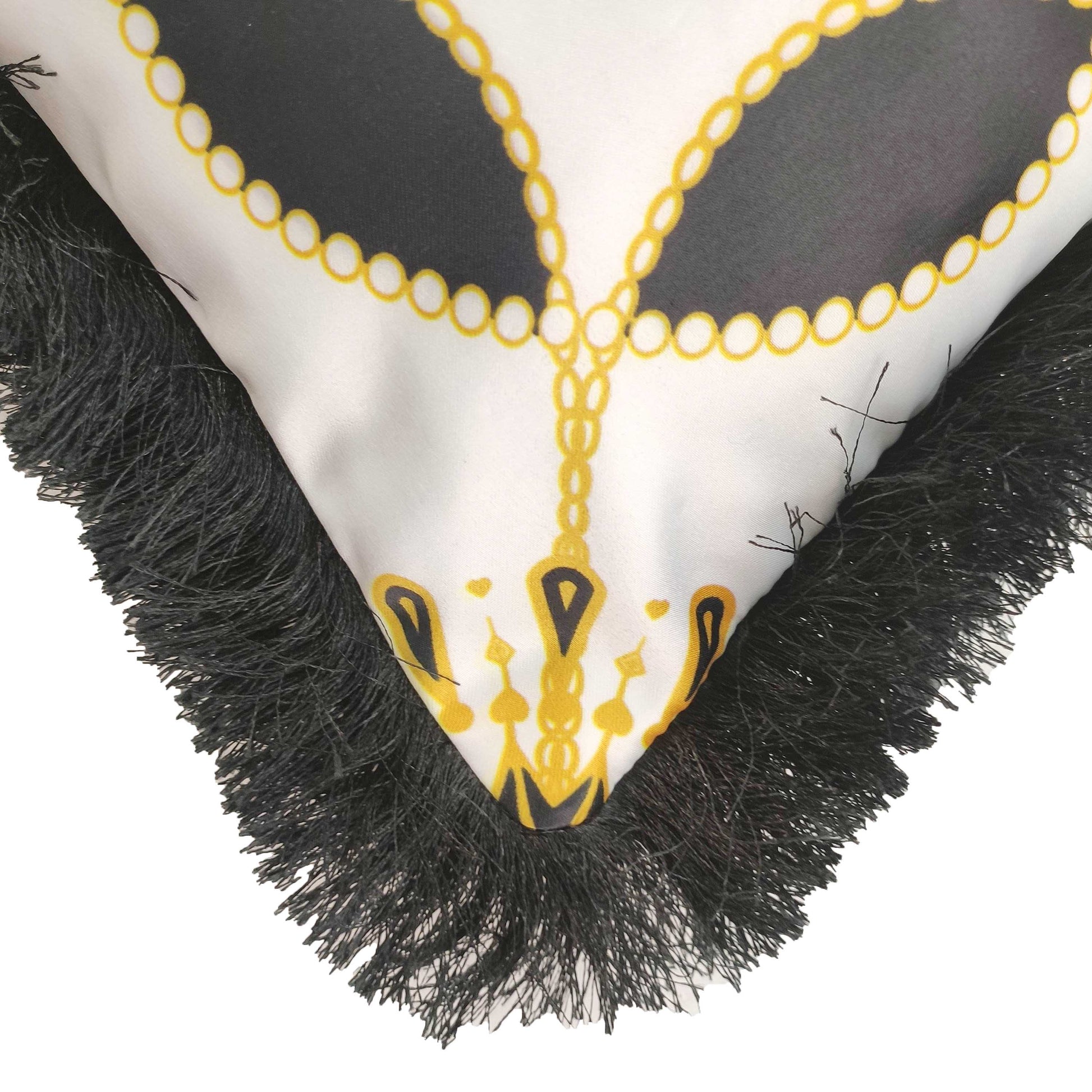 The Cushion With Filler Multi Color CS-055 by RAMSHA HOME features a white fabric with black and yellow chain-like patterns, ornamental details, and black fringe along the edge.