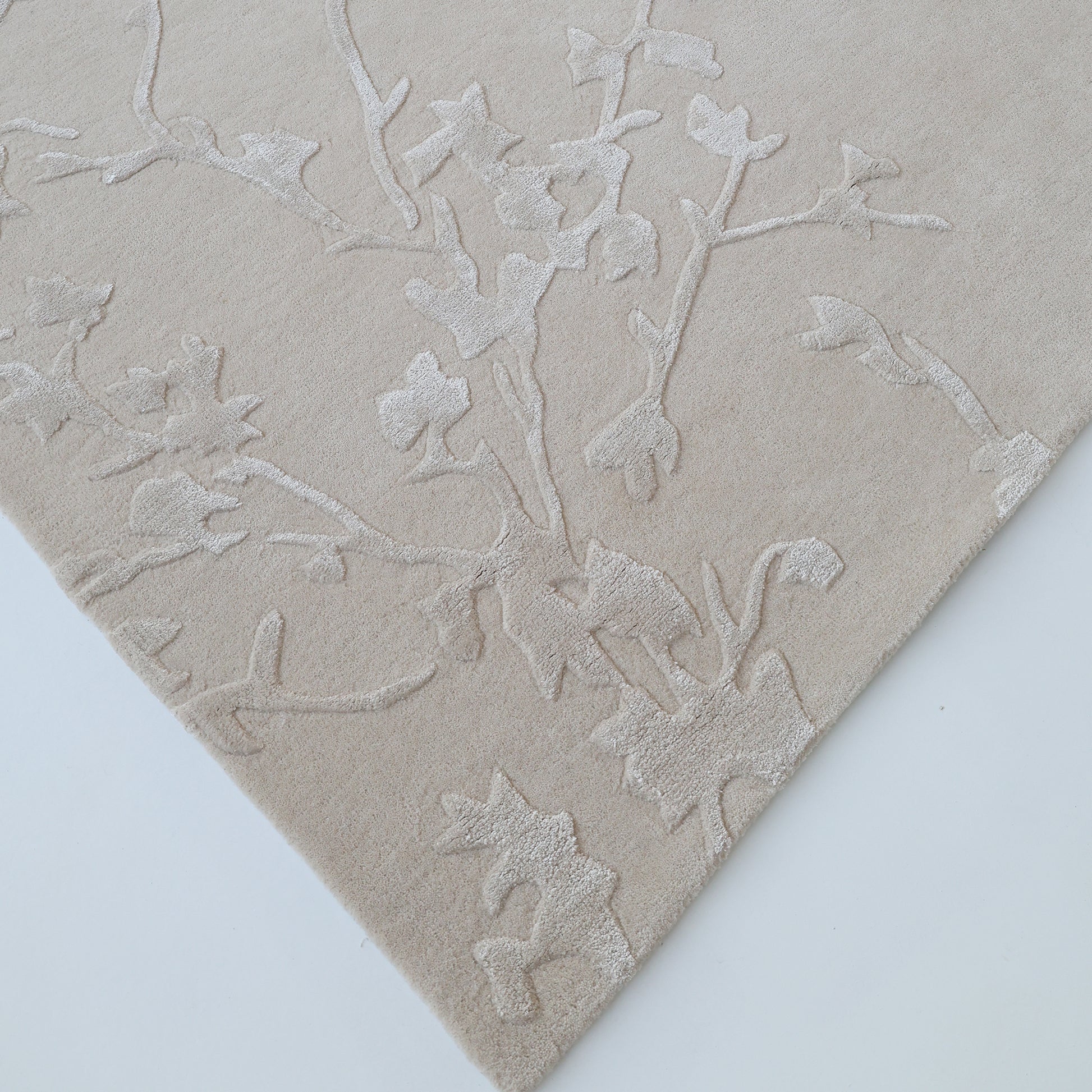 A close-up of the Handmade beige Color Decor Rug- HTWV 115 by RAMSHA HOME shows its raised, textured botanical pattern in matching beige tones, highlighting the hand-tufted wool craftsmanship at the corner.