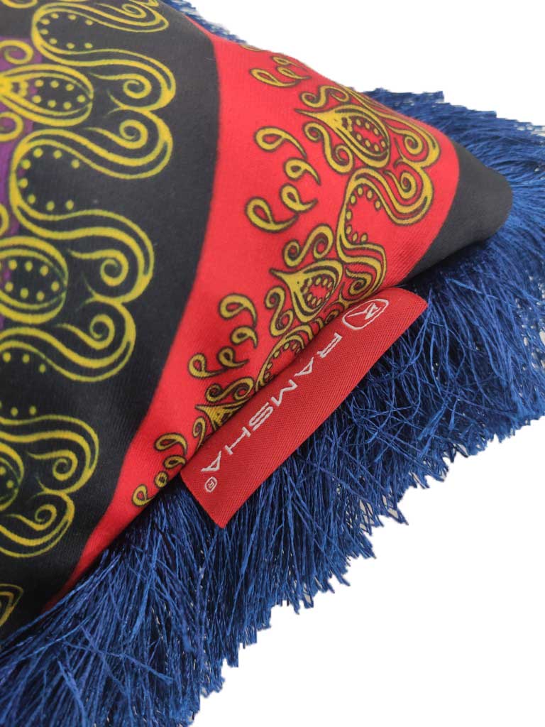 A close-up of the RAMSHA HOME Polyester Home Decor Cushion With Filler CS-054, featuring a red and black patterned fabric with yellow accents, blue fringe trim, fluffy filler, and a red "RAMSHA" tag—ideal for modern homes.