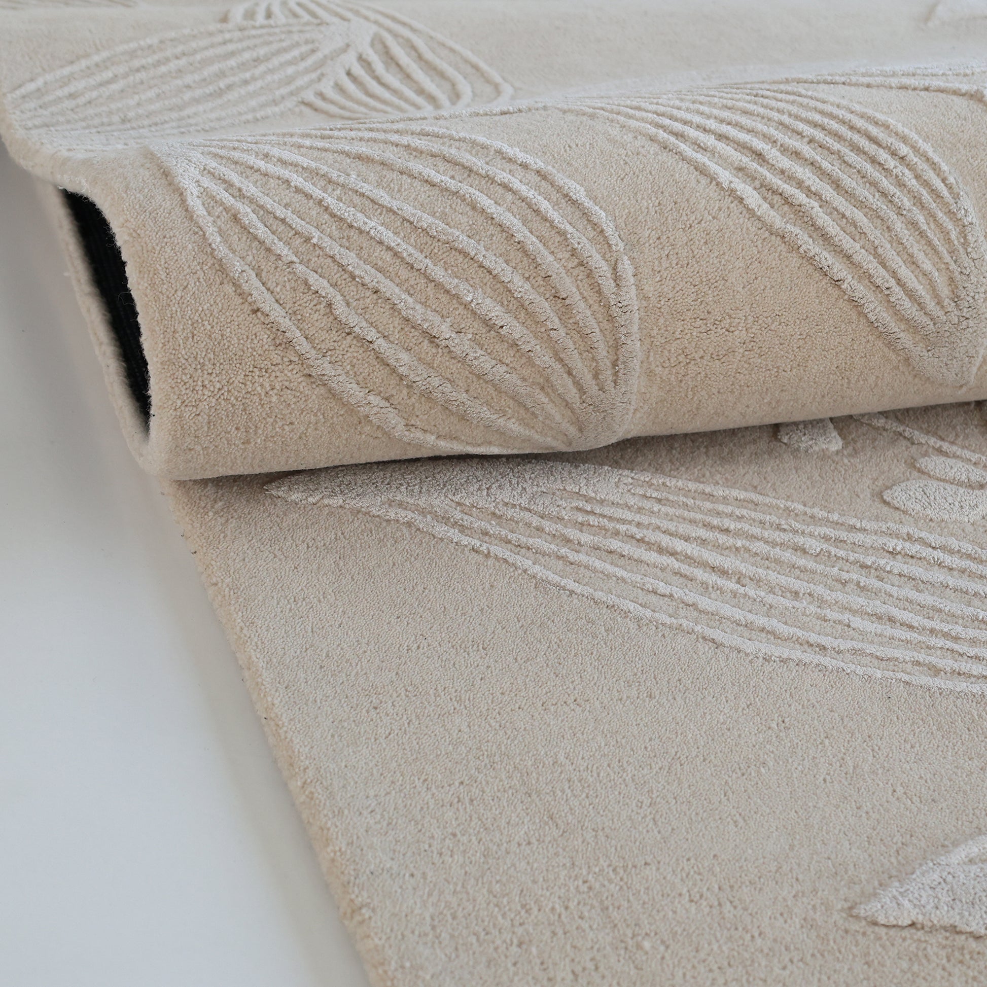 A close-up of the RAMSHA HOME Natural Beige & Ivory Handmade Area Rug (HTWV-146), hand-tufted with a raised leaf pattern, partially rolled on a white surface.