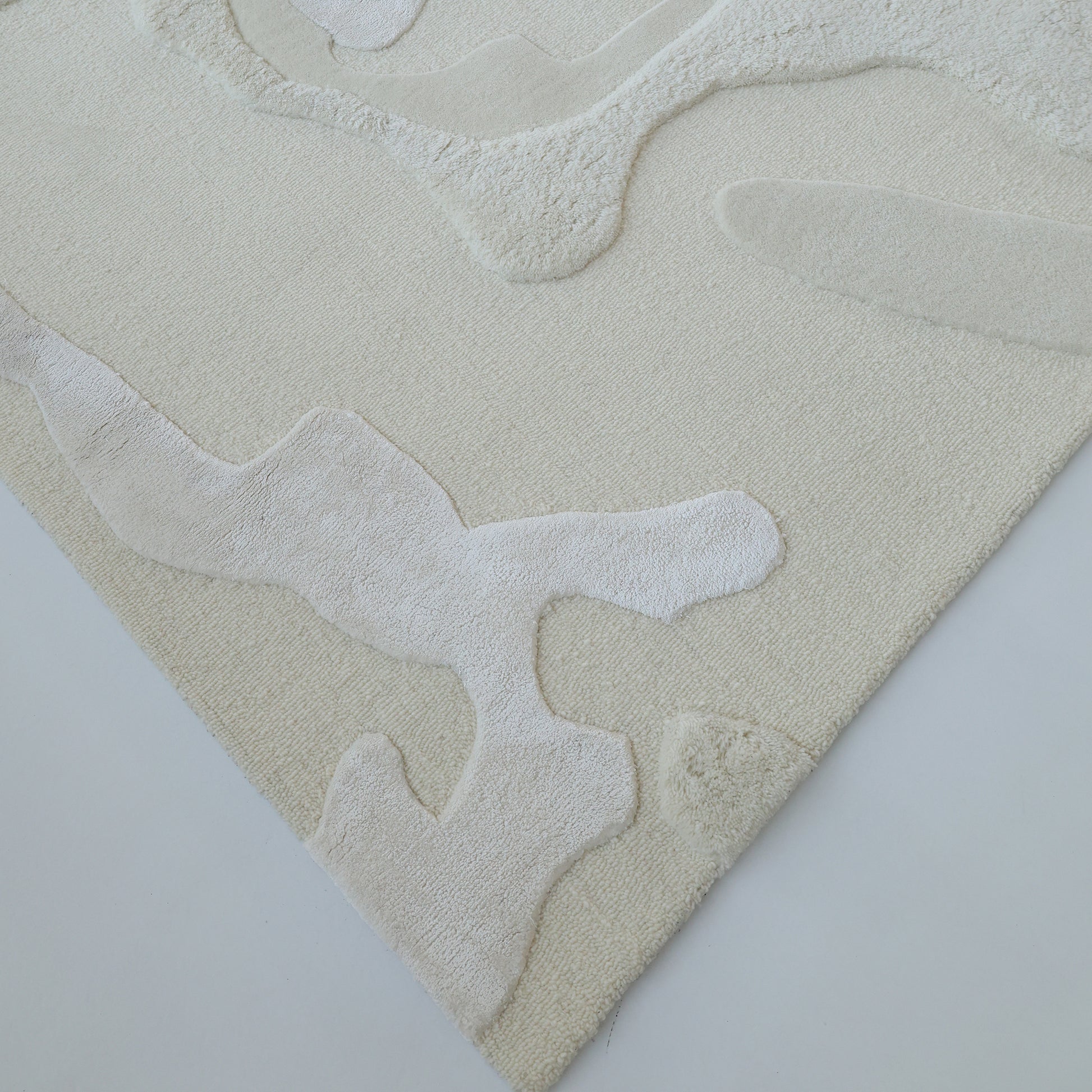 The RAMSHA HOME Handcrafted Natural White Area Rug – HTWV-129 features abstract, raised patterns and organic shapes in light beige, shown close-up against a white background.