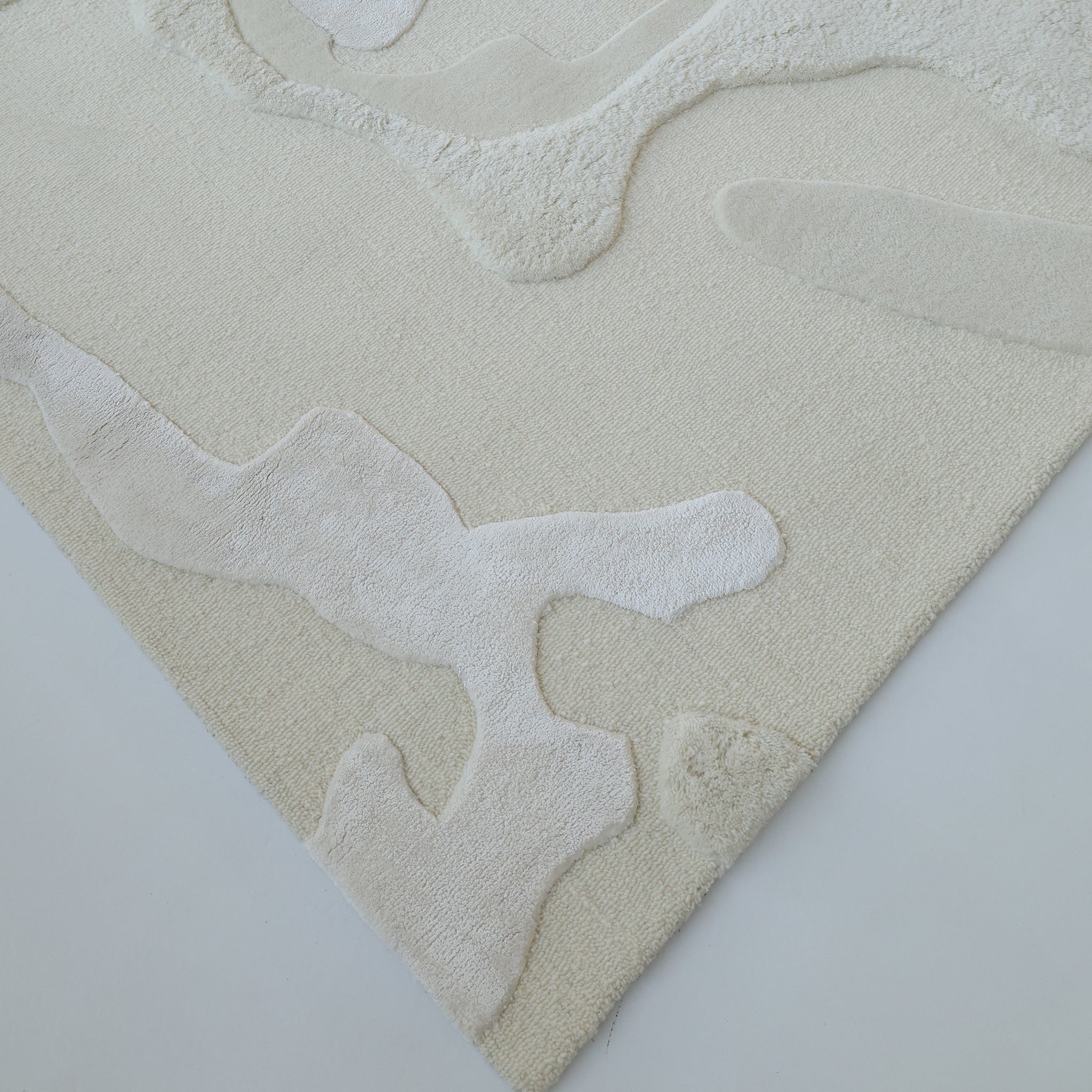 The RAMSHA HOME Handcrafted Natural White Area Rug – HTWV-129 features abstract, raised patterns and organic shapes in light beige, shown close-up against a white background.