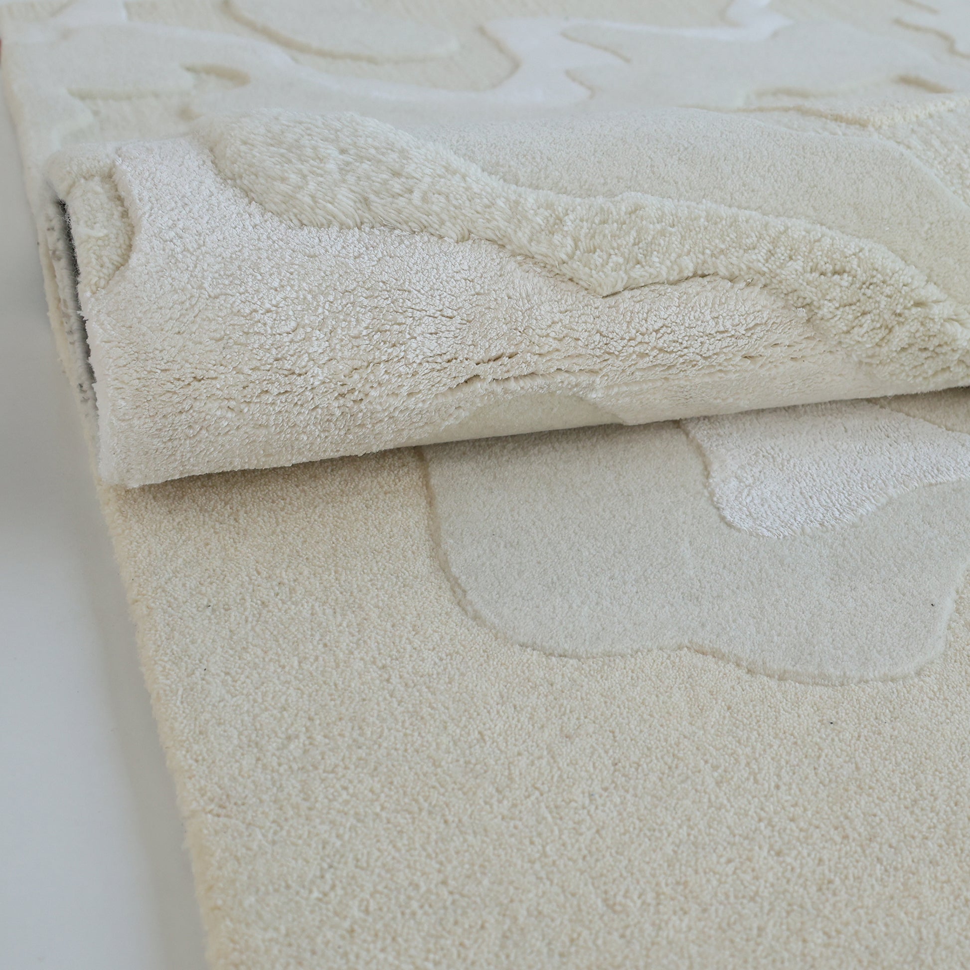 A close-up of RAMSHA HOME's Handcrafted Natural White Area Rug – HTWV-129, featuring a cream shade with raised abstract patterns and a soft, plush handtufted surface, displayed on a matching flat surface.