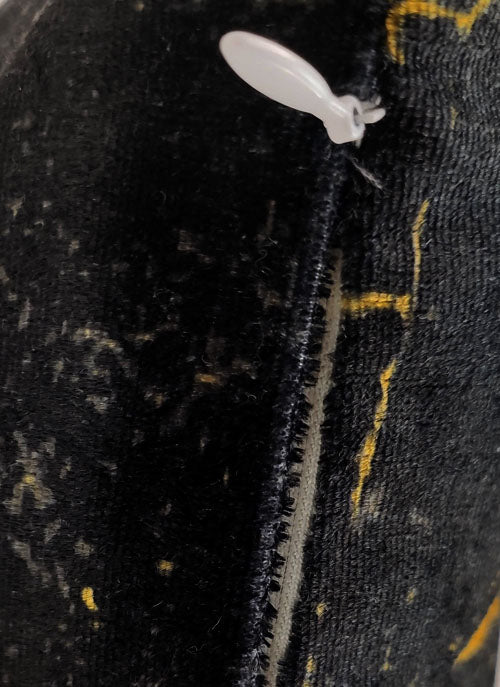 Close-up of the RAMSHA HOME Polyester Cushion Cover in black with yellow and white patterns, featuring a visible seam and a white plastic tag fastener near the edge.