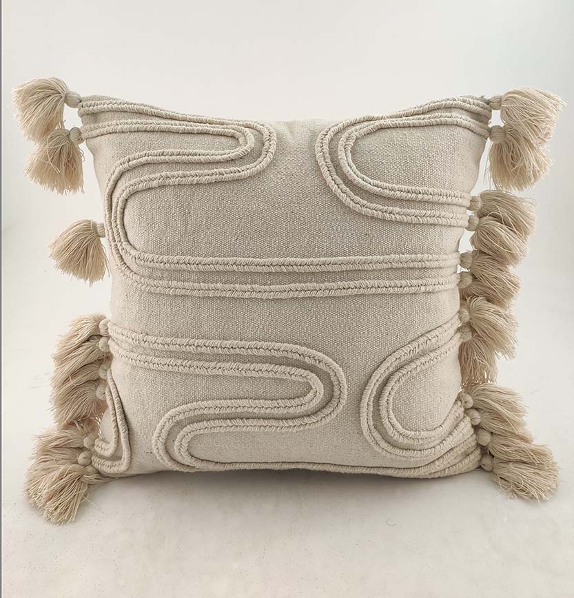 The RAMSHA HOME Cotton & Polyester Natural & White Color Cushion With Filler CS-009 features a beige square design with wavy embroidered patterns and tassels, displayed against a plain white background.