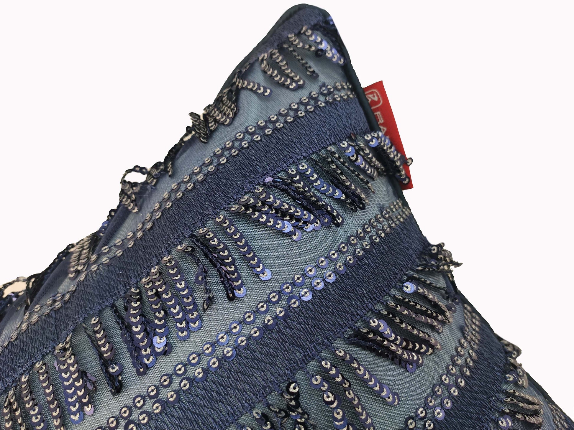 A close-up of the RAMSHA HOME Modern Polyester Cushion Cover in blue, showcasing horizontal sequin stripes and textured fringe. A small red fabric tag is visible at the top edge against a plain white background.
