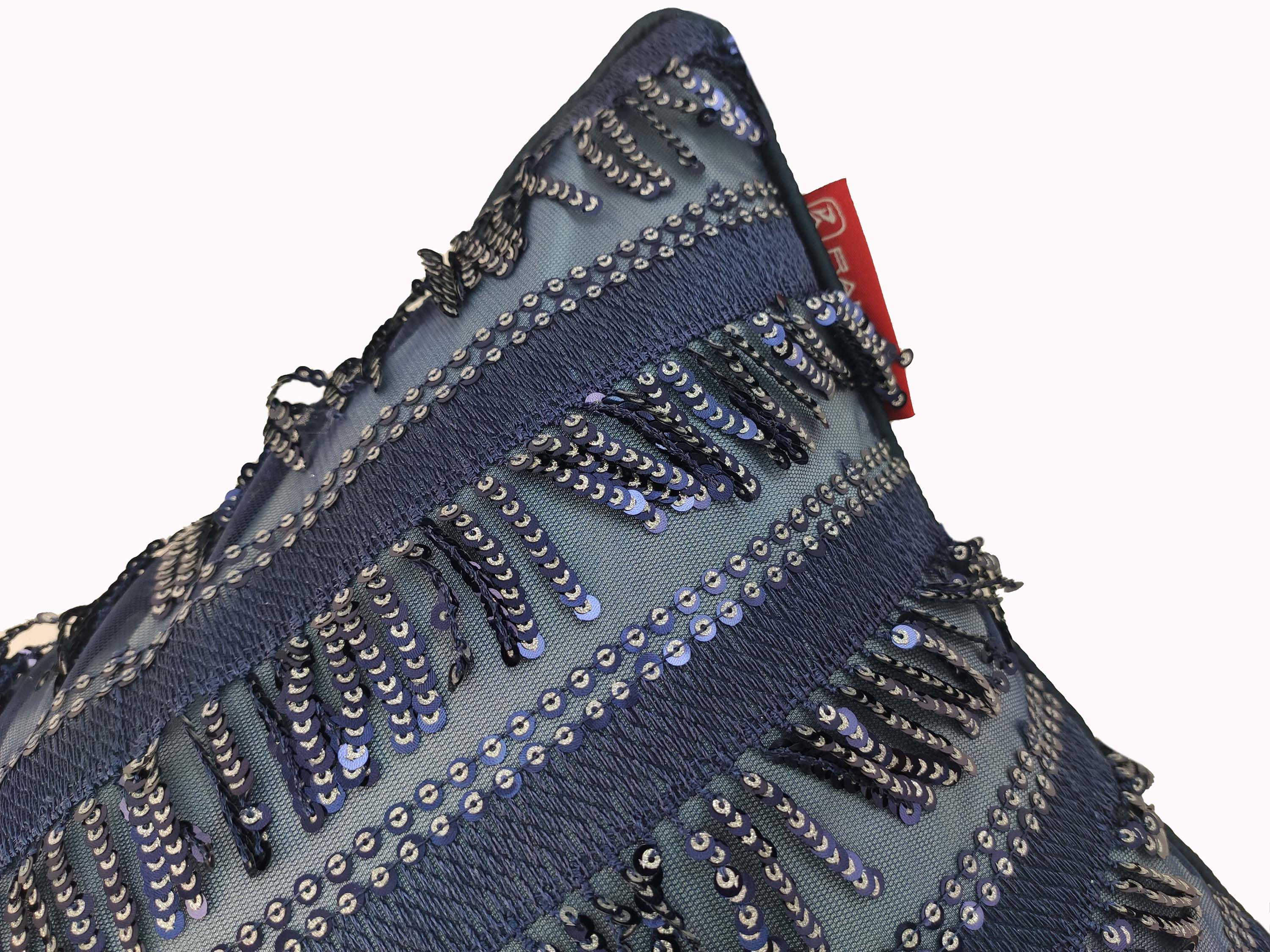 A close-up of the RAMSHA HOME Modern Polyester Cushion Cover in blue, showcasing horizontal sequin stripes and textured fringe. A small red fabric tag is visible at the top edge against a plain white background.