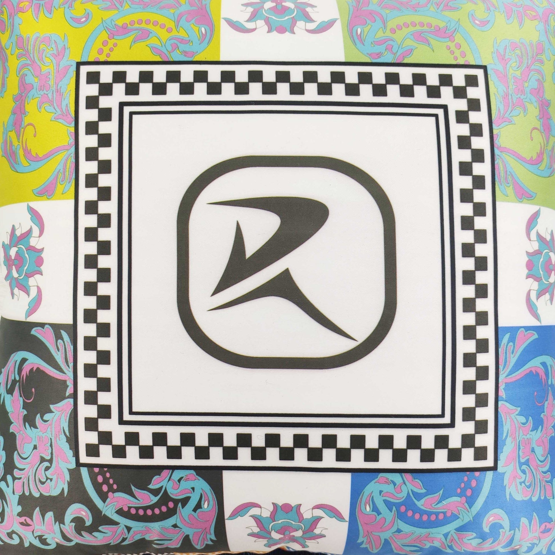 The RAMSHA HOME Polyester Cushion Multi Color CS-058 features ornate floral and checkered patterns with a bold abstract “R” logo on white, making it an ideal decorative accent for any space.
