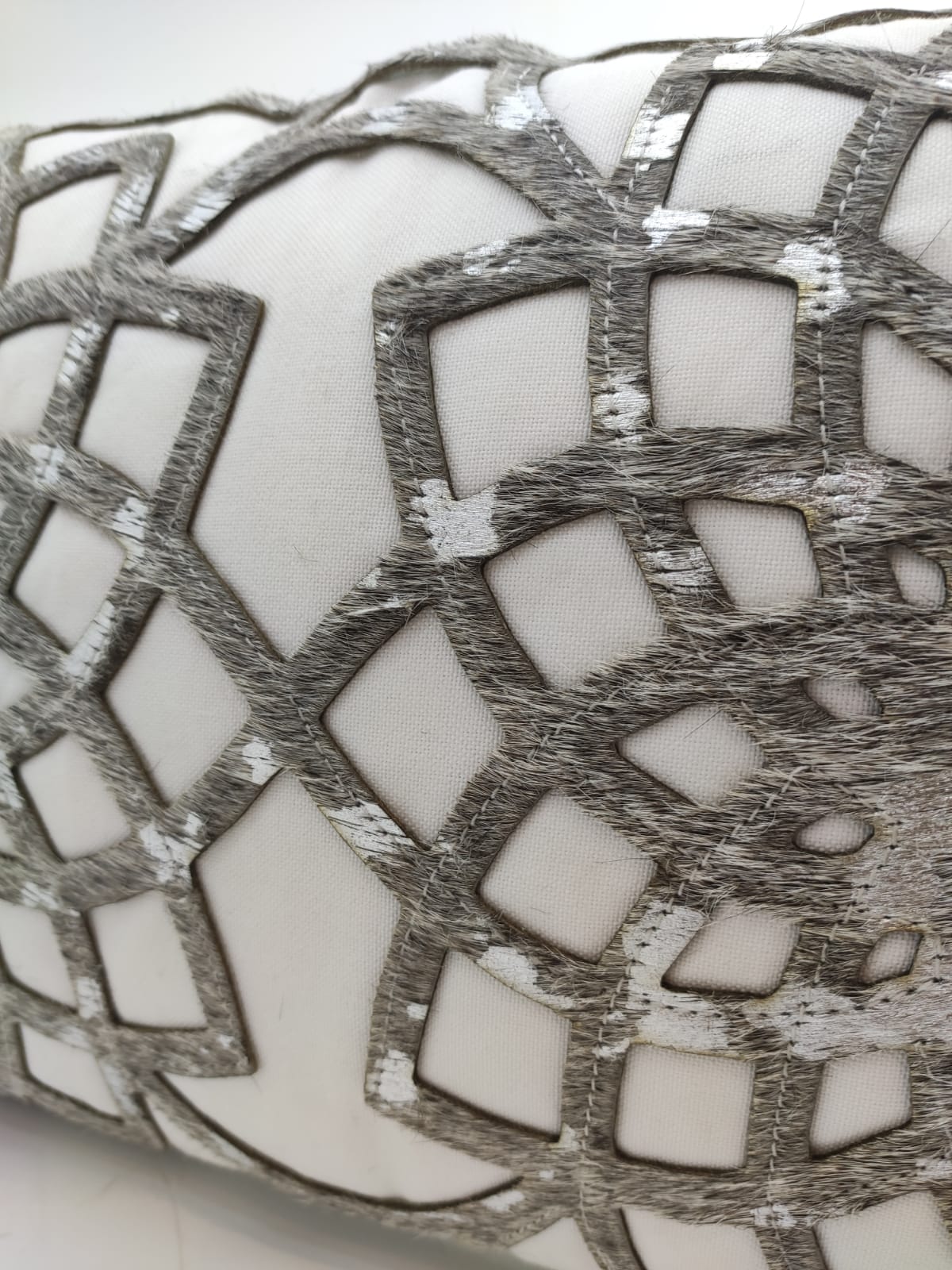 Close-up of RAMSHA HOME's CS-102 Leather Cushion: a premium white pillow adorned with an intricate silver and gray geometric embroidered pattern, featuring intersecting shapes and metallic accents.