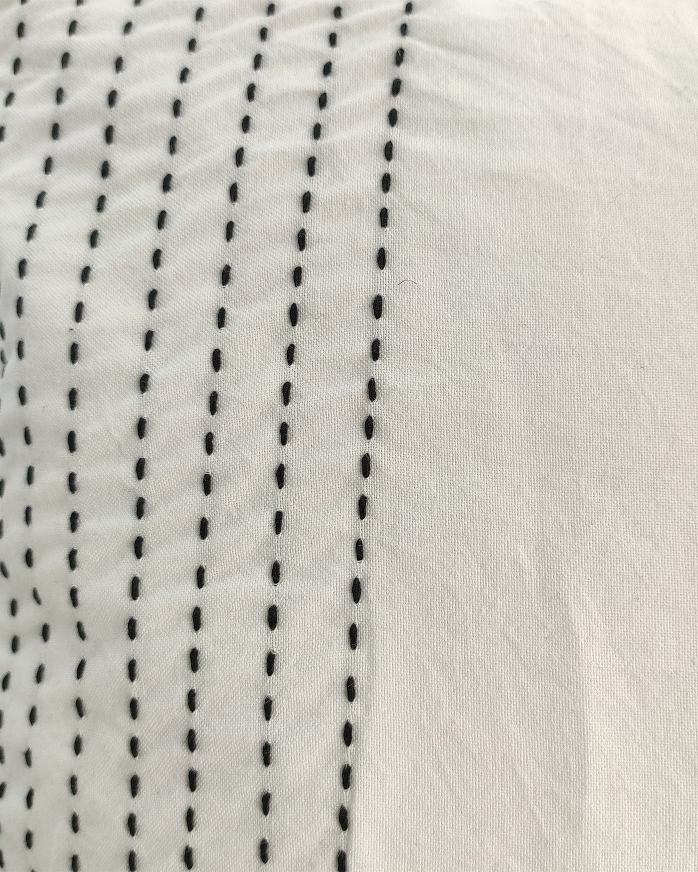 Close-up of the RAMSHA HOME Embroidery White And Black Cotton Cushion With Tassel CS-190, featuring evenly spaced black dashed lines in vertical rows on smooth white fabric, with raised stitching for a simple, modern look.