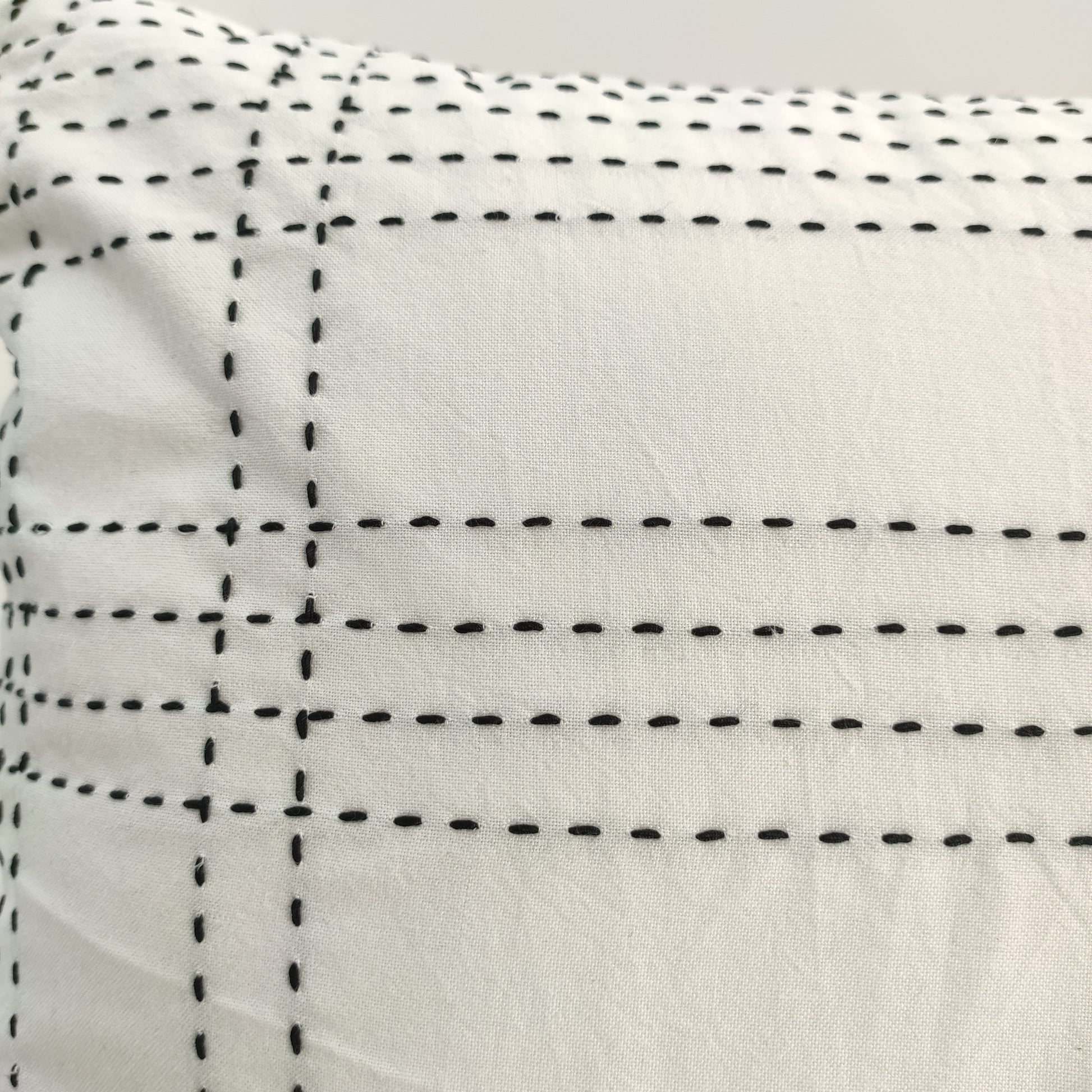 The RAMSHA HOME Embroidery White And Black Cotton Cushion With Tassel CS-193 features a minimalist grid pattern with black dashed lines on white fabric, adding a geometric touch to your home décor.