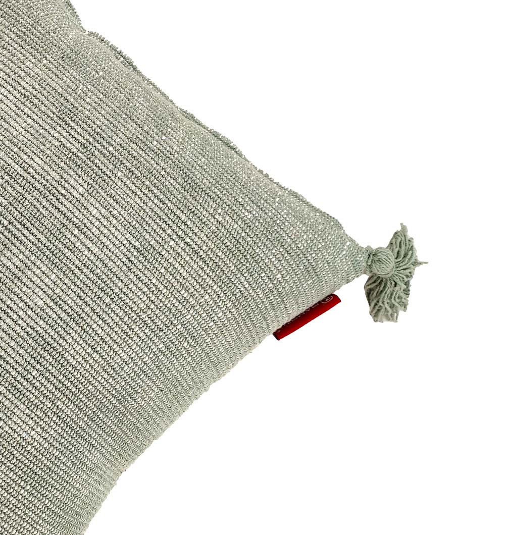 A close-up of the RAMSHA HOME Cotton Cushion With Fringes CS-133 in light green, featuring a corner tassel, a small red fabric tag by the tassel, and a high-quality filler for extra comfort.