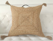 The RAMSHA HOME Jute Cotton Cushion With Tassel And Handle CS-195, featuring a braided texture and corner tassels, is displayed on a white, tufted sofa.