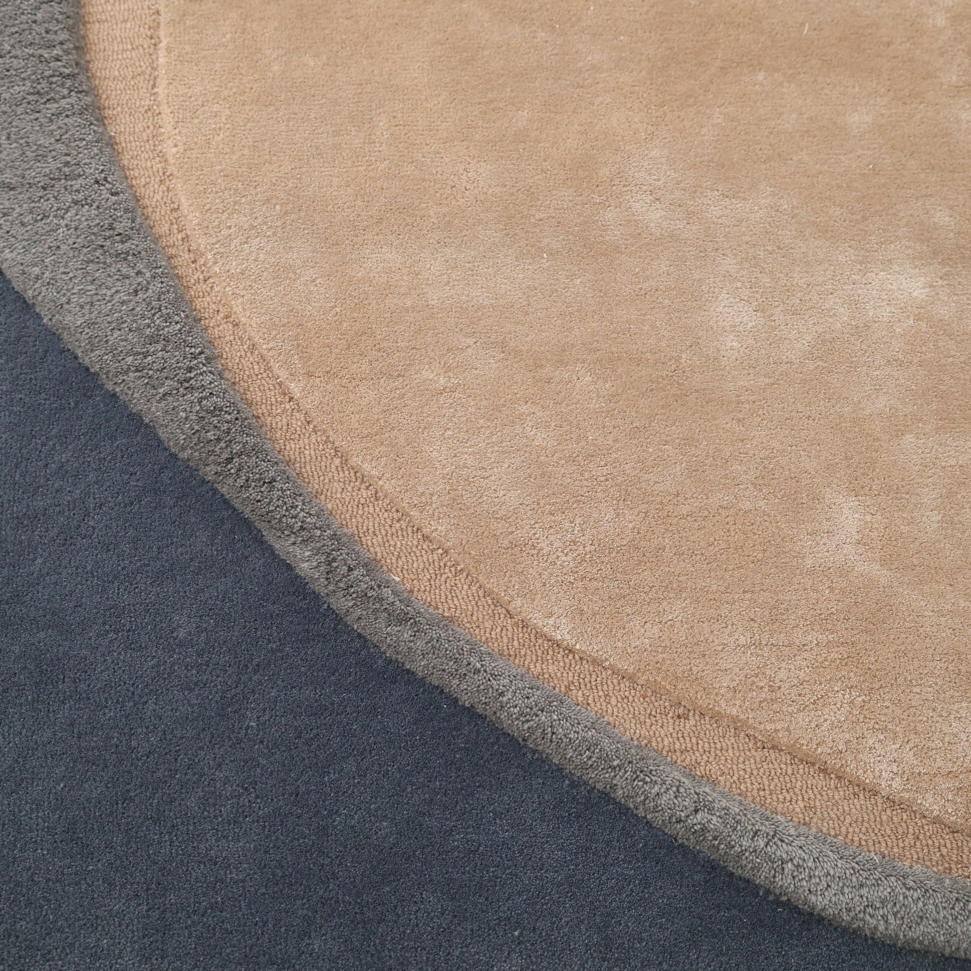 Close-up of the RAMSHA HOME Oval Shape Home Decor Multi Color Rug HTWV-90, featuring hand-tufted abstract sections: a large tan area, smaller gray border, and dark blue background, all with a soft textured surface.