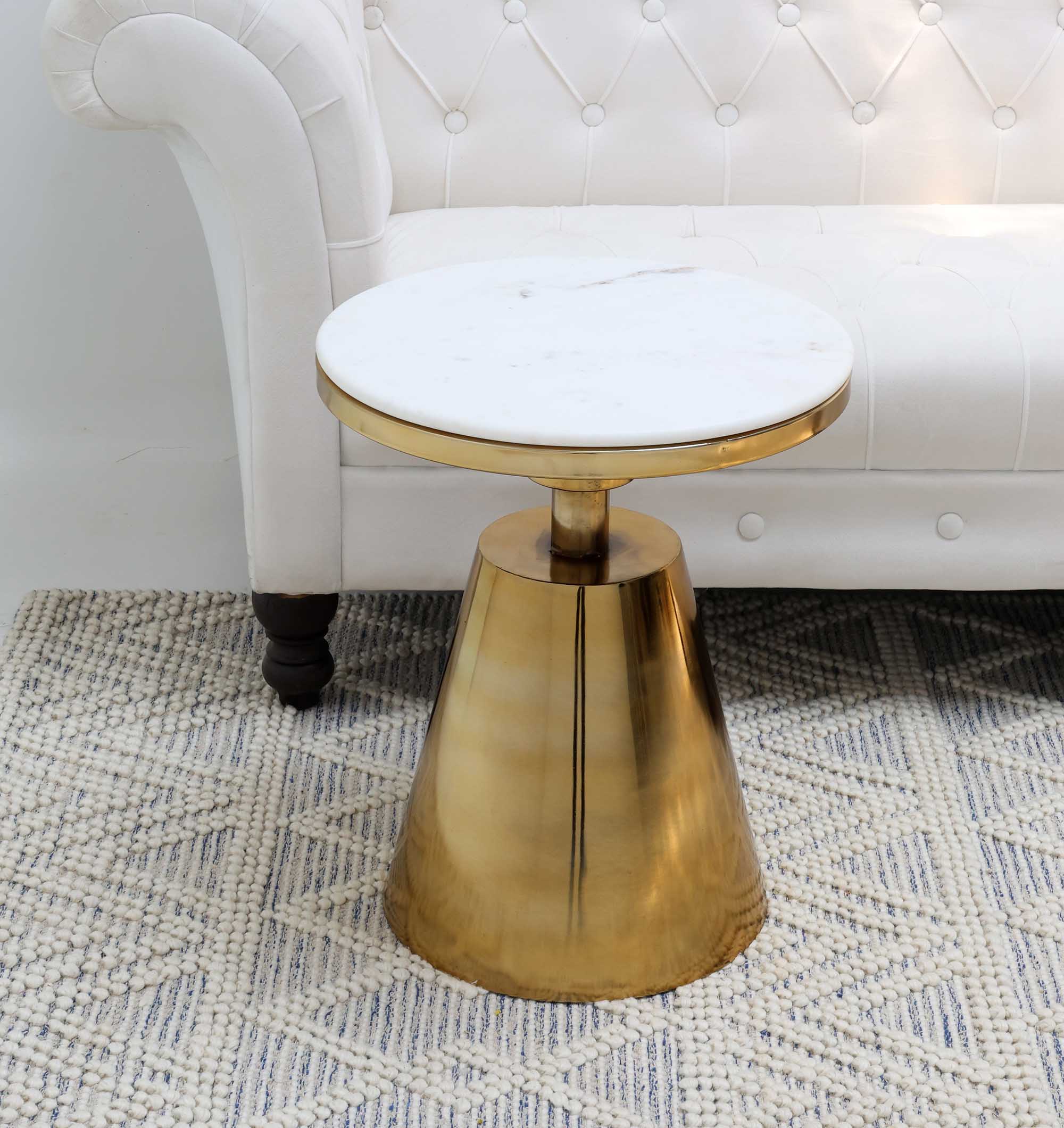 The RAMSHA HOME Aurelia Luxe Marble & Iron Accent Table AD25-26, featuring a white marble top and shiny gold conical base, sits on a textured rug beside a white tufted sofa.