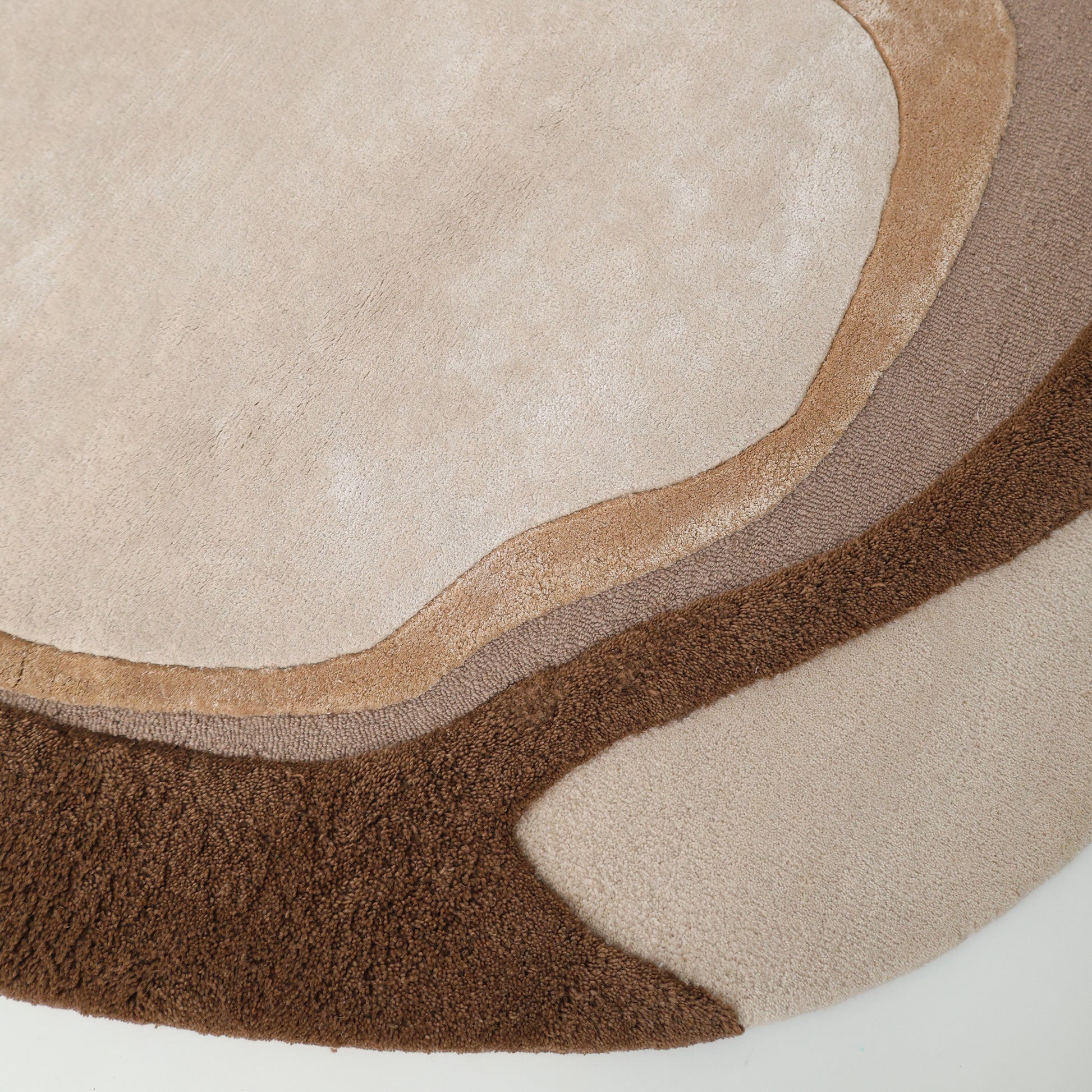 Close-up of the Vibrant Round Shape Handmade Rug - HTWV 95 (200 cm) by RAMSHA HOME, featuring hand-tufted wool in beige, tan, and brown curved layers with a textured surface—an elegant neutral area rug with organic shapes.
