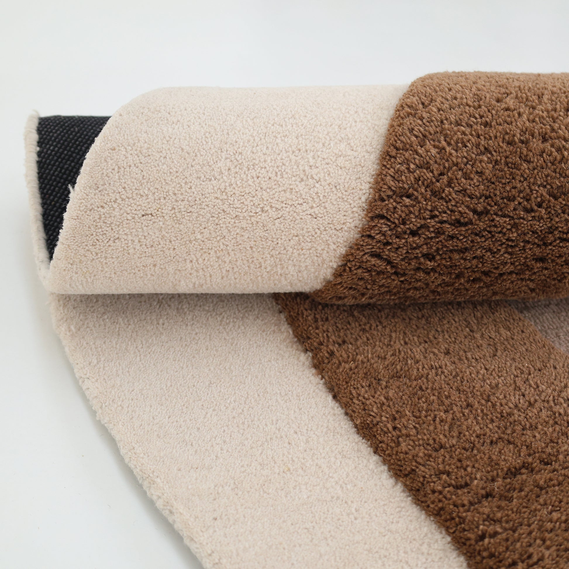 A close-up of the RAMSHA HOME Vibrant Round Shape Handmade Rug - HTWV 95 (200 cm) highlights its plush, hand-tufted wool texture with beige and brown sections and layered fabric, set against a white background.