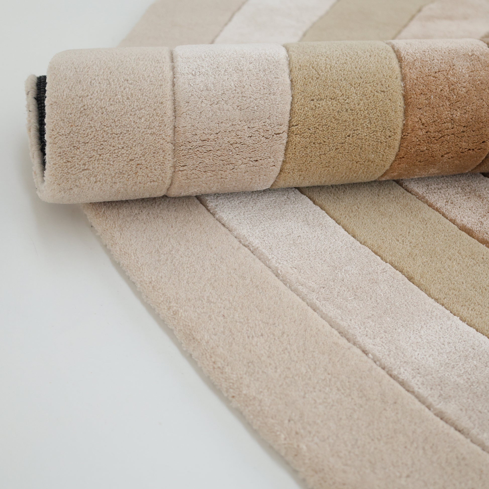 A close-up of the RAMSHA HOME Vibrant Living Room Handmade Rug (HTWV-81 B, 200x300cm), hand tufted in soft wool with horizontal beige, tan, and brown stripes, highlights its plush texture on a light surface.