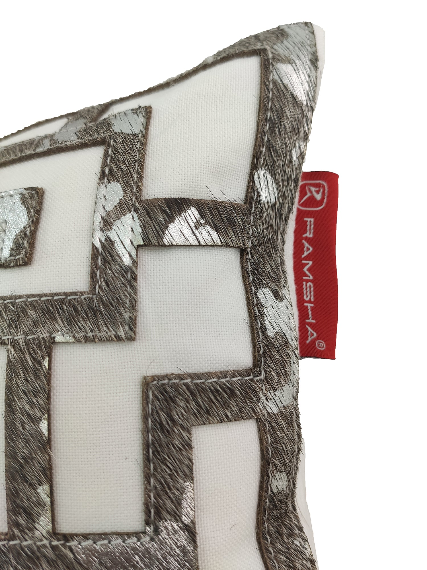 A close-up of the Modern Cushion CS-107 by RAMSHA HOME—a white cushion with a silver geometric embroidered pattern and a red fabric tag, blending superior comfort with contemporary style.