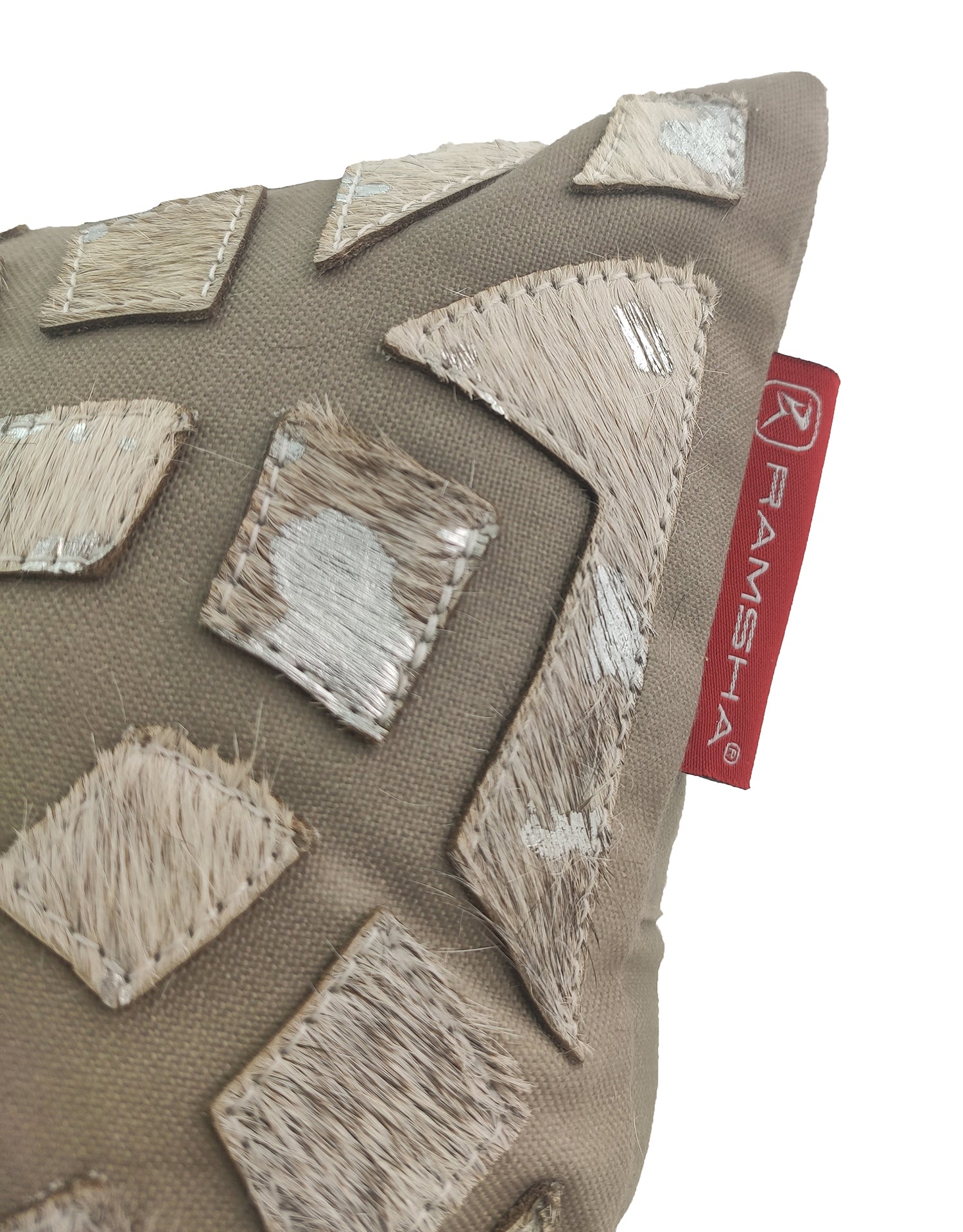 A close-up of the RAMSHA HOME Decorative Cushion CS-105, made from polyester and leather, with textured light brown and cream geometric patches and a red side tag labeled RAMSHA.