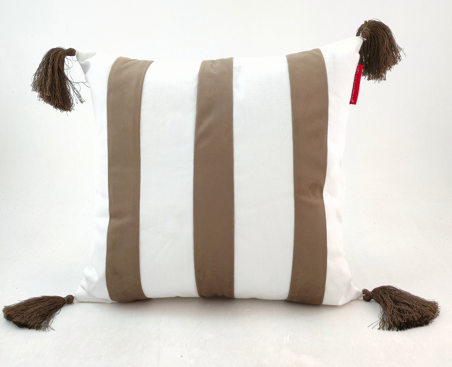 The RAMSHA HOME White & Brown Cushion CS-138 is a stylish white polyester cushion with three vertical beige stripes and brown tassels at each corner, adding both elegance and durability to your home decor.