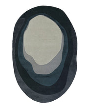 The Handmade Layered Abstract Shaped Rug HTW 131 (200 x 300 cm) from RAMSHA HOME features an eye-catching oval, irregular design with layered abstract forms in sophisticated shades of gray and blue. Reminiscent of watercolor artwork or flowing topographic lines, this modern area rug is hand tufted for a luxurious feel, making it a striking addition to any contemporary space.