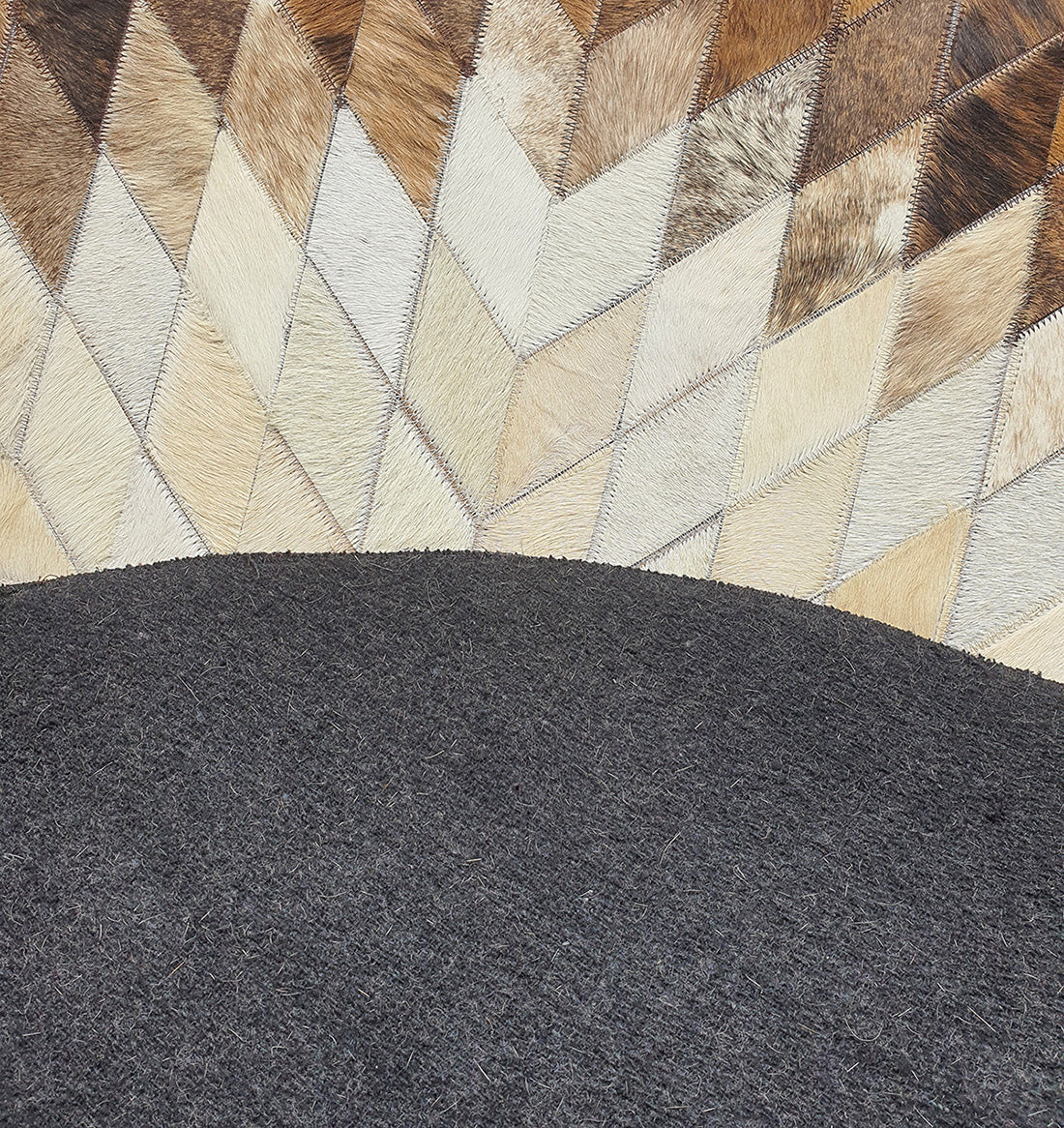 A curved section of dark leather contrasts with light brown, tan, and cream chevron patches on the RAMSHA HOME Multi Color Home Decor Round Leather Rug - LR 017, evoking the look of animal hide.