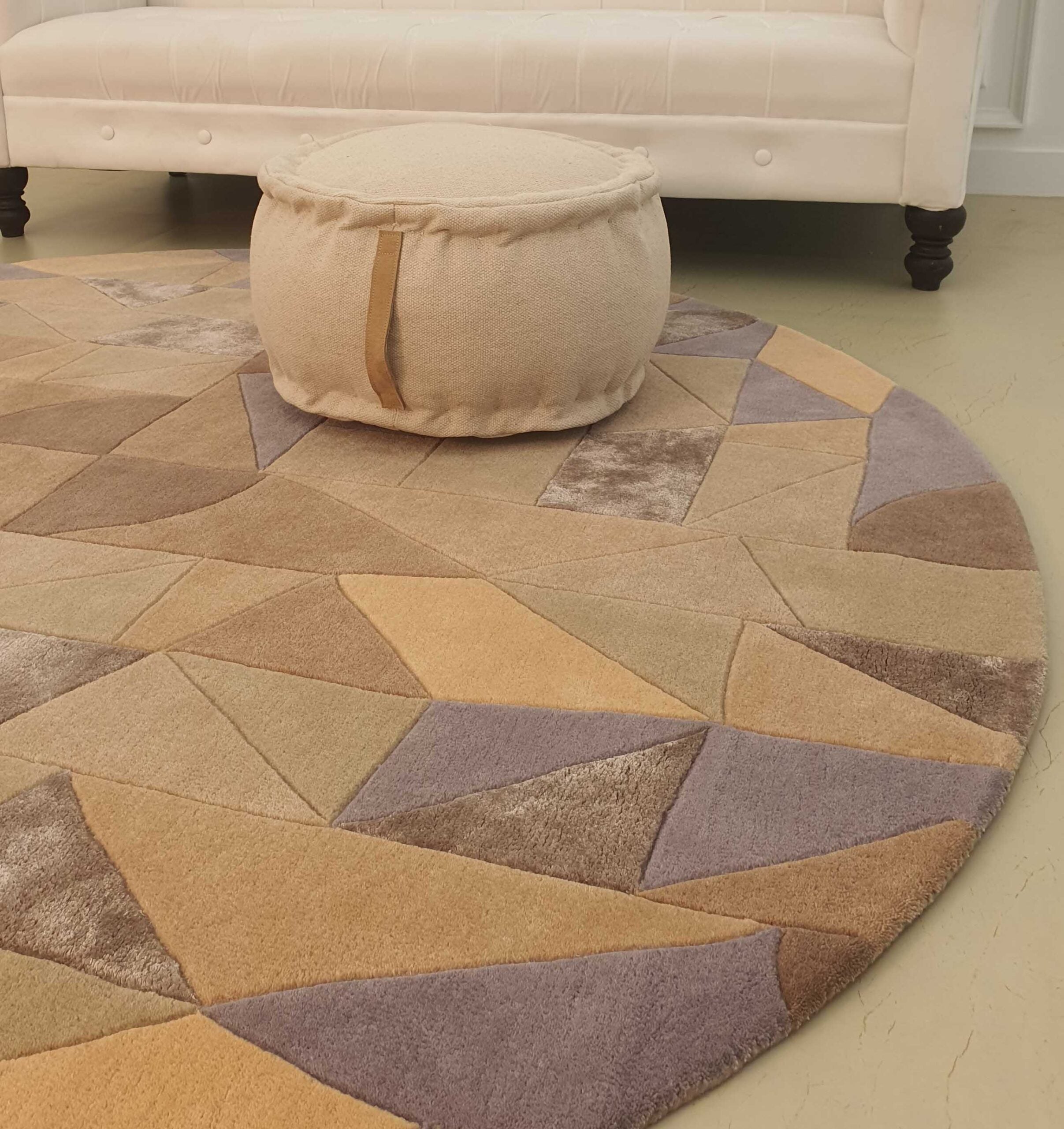 The RAMSHA HOME Vibrant Multi Color Round Handmade Rug - HTWV 50 (200cm) with a geometric design sits on the floor, while a cream pouf and a white tufted sofa can be seen in the background.